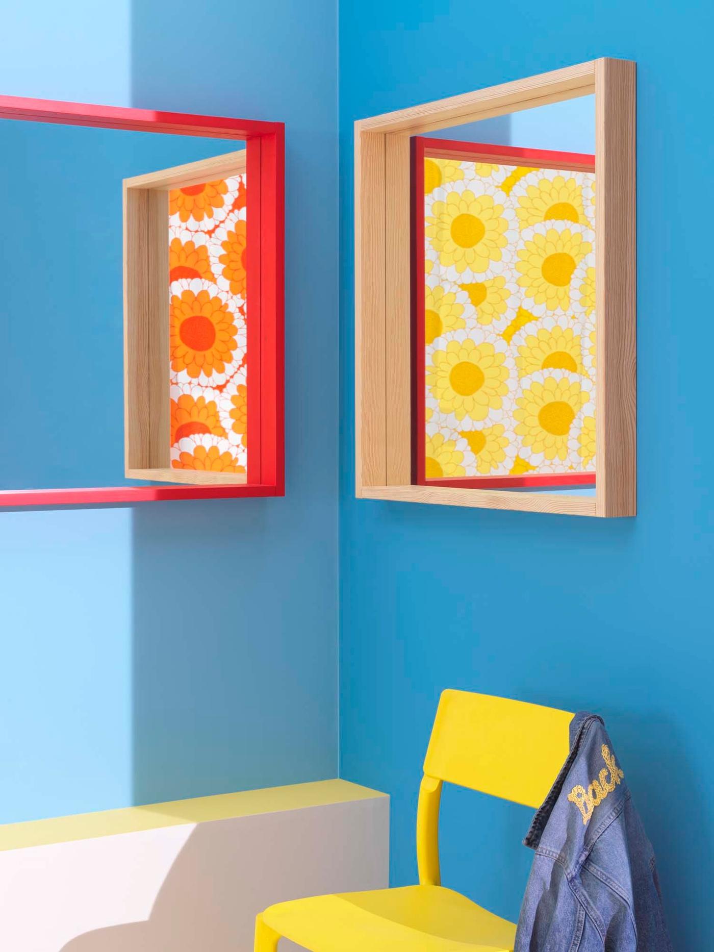A red mirror and a natural mirror face eachother on 2 walls. A yellow chair sits below.
