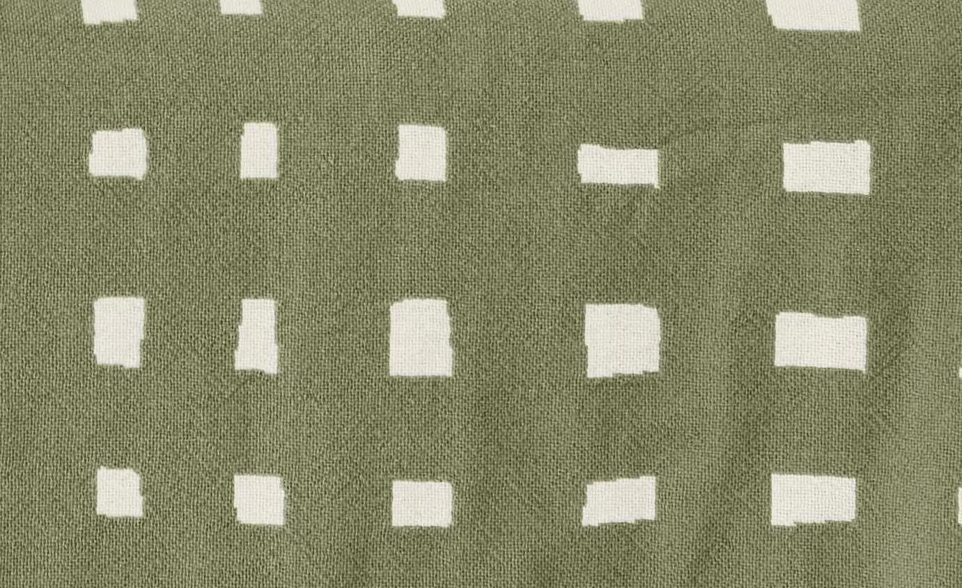 A close-up of a green throw with cream rough squares.