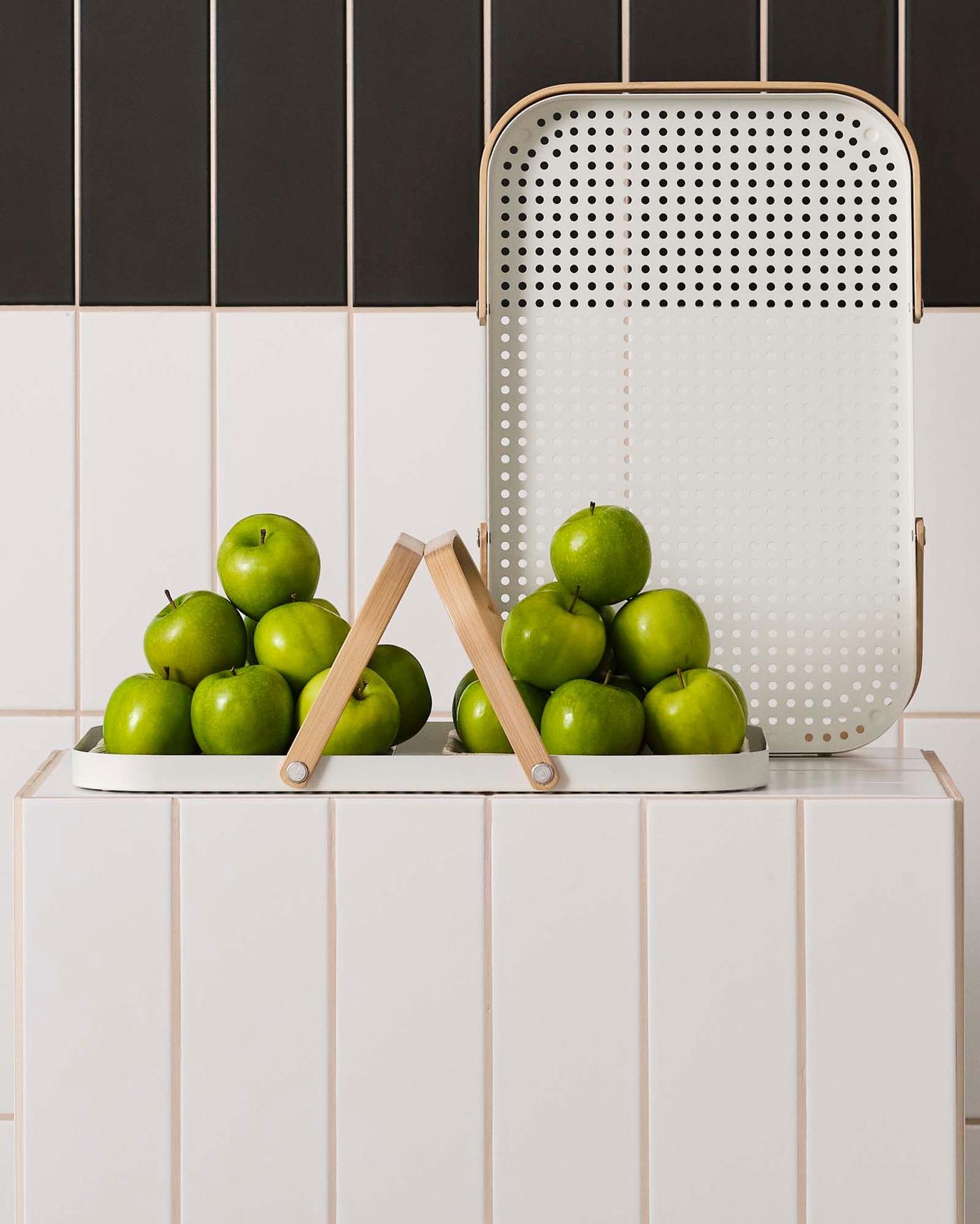 A white tray stacked with limes stands on and in front of white and black tiles.