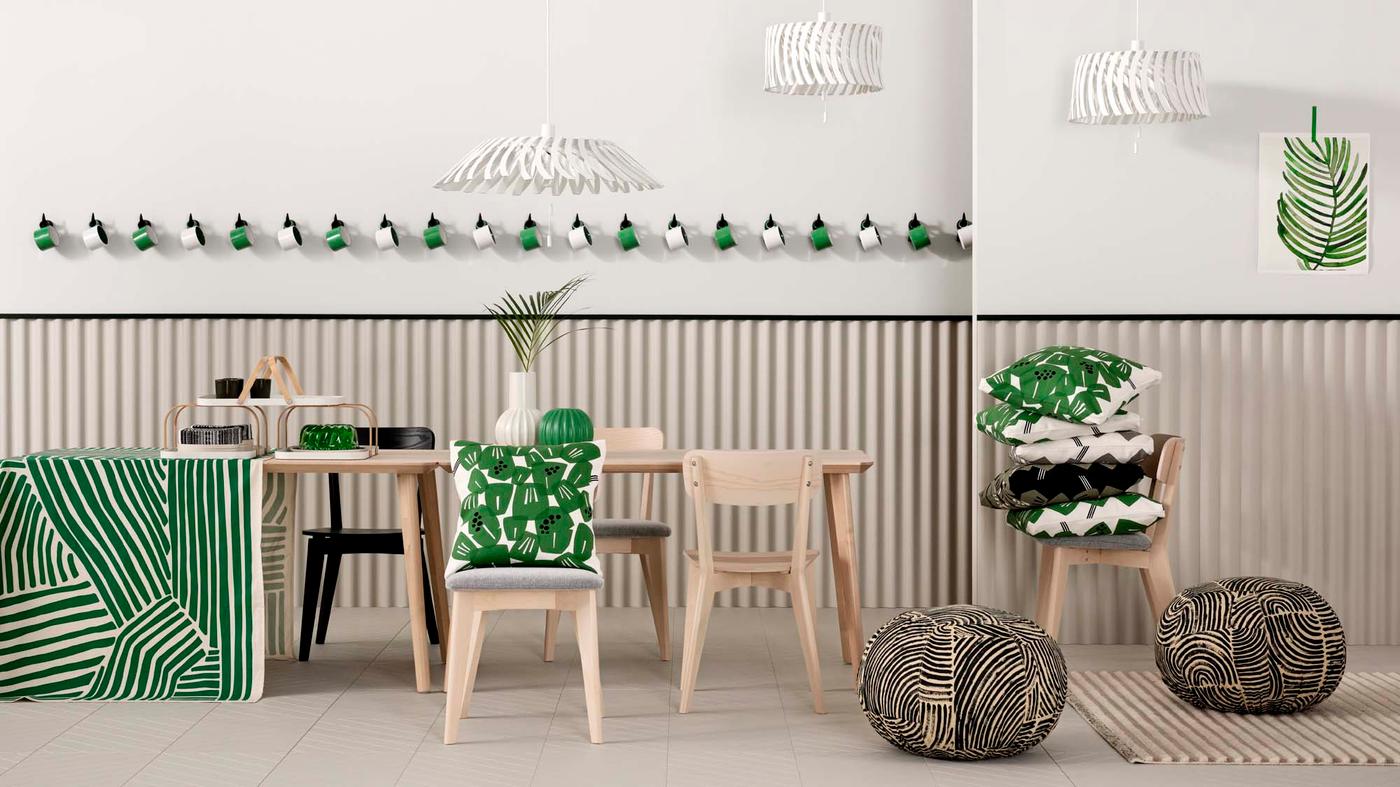 A dining room table and chairs stacked with green, black and white cushions, against a striped background.