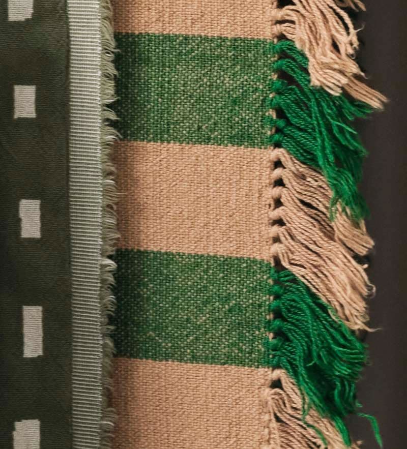 A close-up of a green and brown fringed throw and an olive and cream fringed throw.