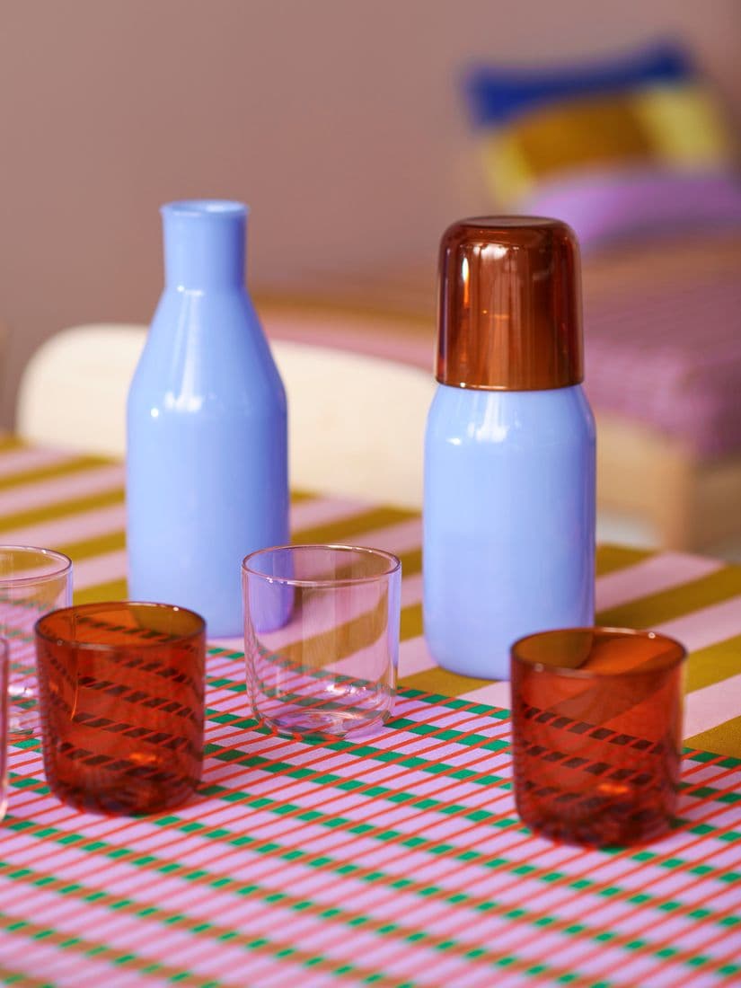 Two blue glass vases stand next to red and transparent glasses, standing on a patterned colourful table cloth