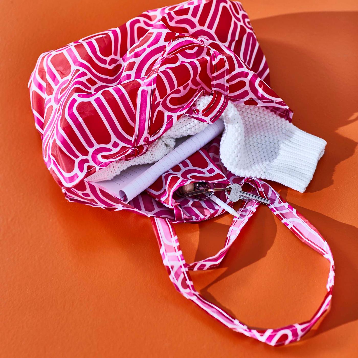 A pink and red bag lays open on an orange surface, revealing its contents.
