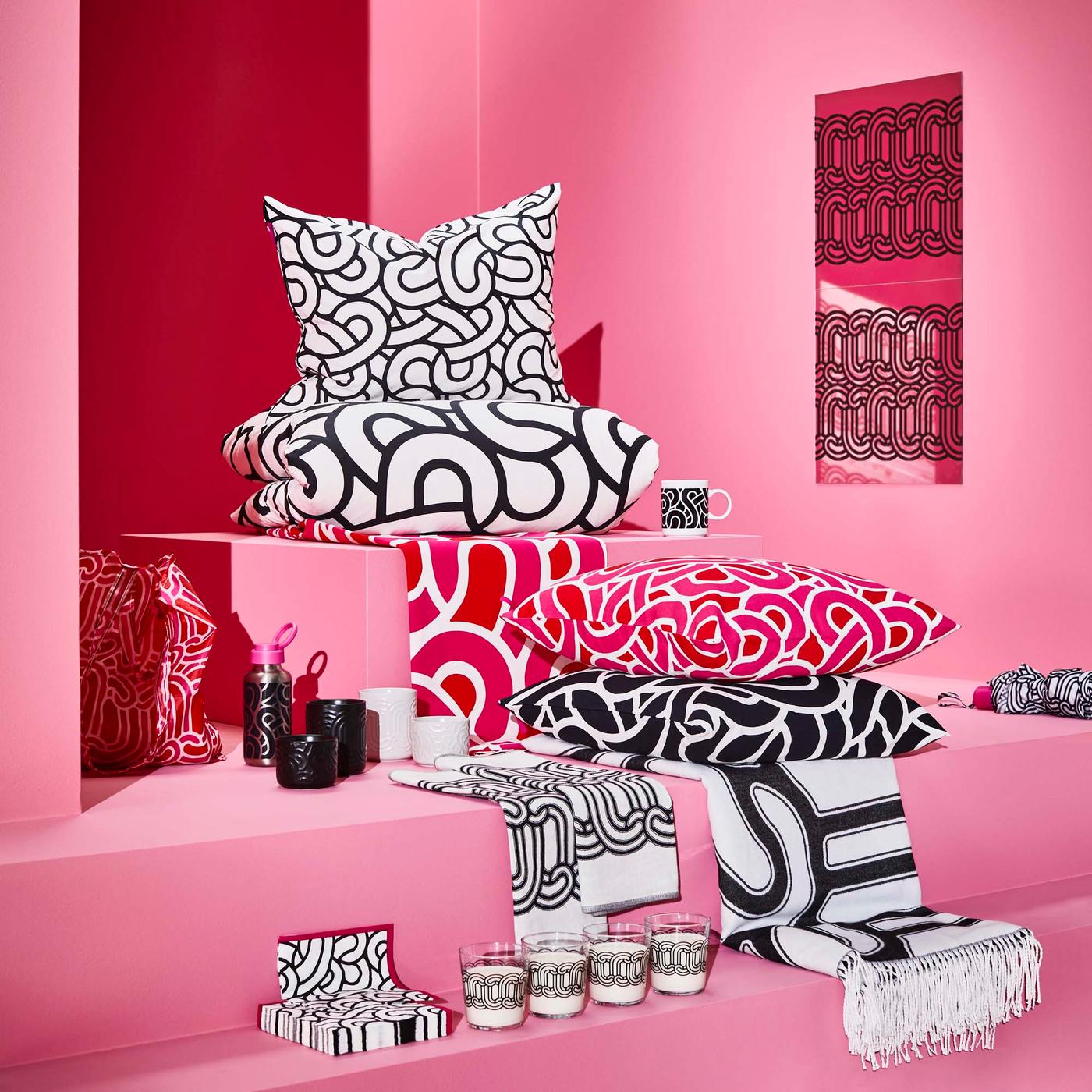 A group of patterned home accessories, such as pillows and napkins, against a pink backdrop.