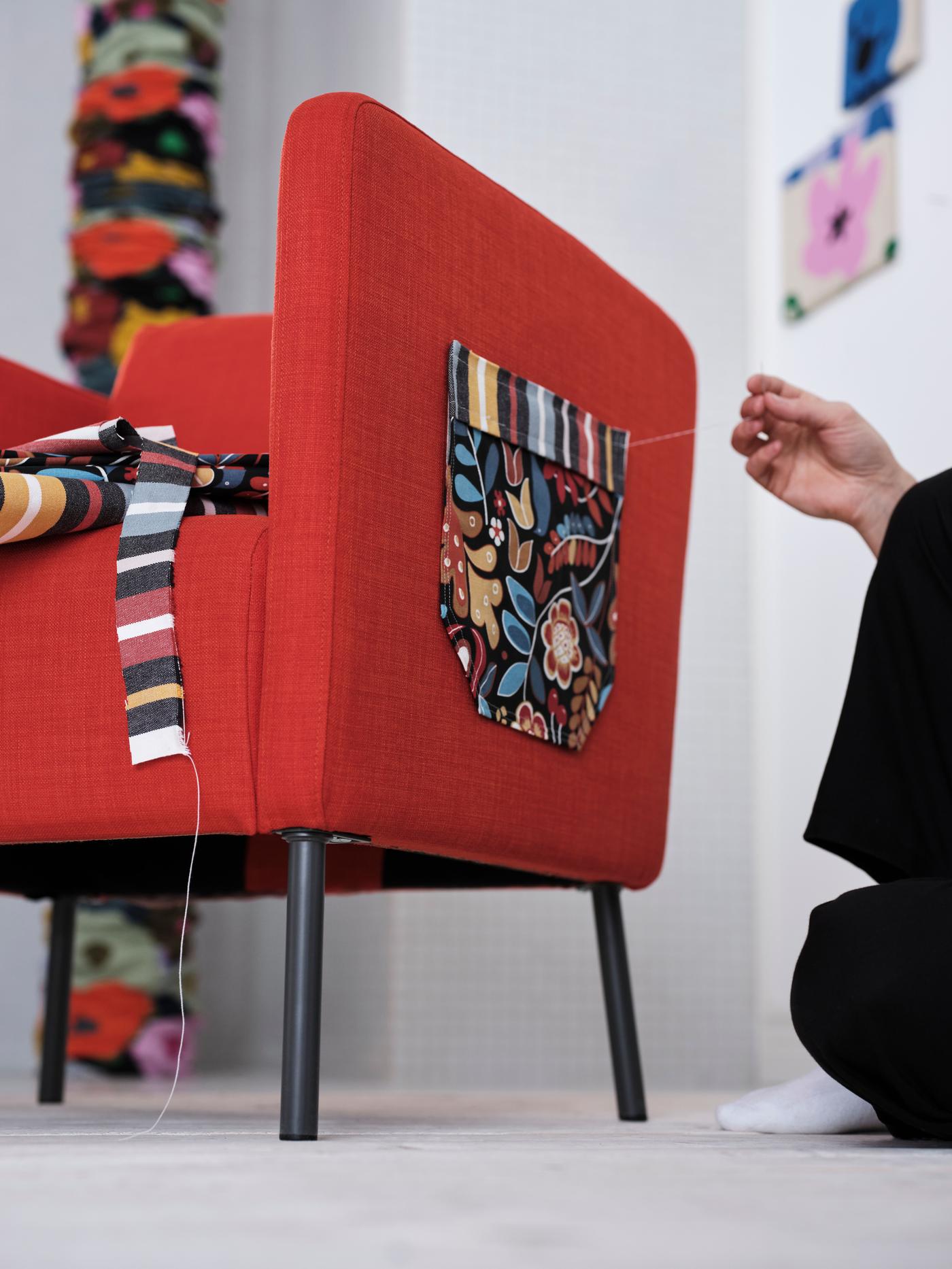 A person is trying to mend the side of a sofa with a piece of fabric with a floral pattern. 