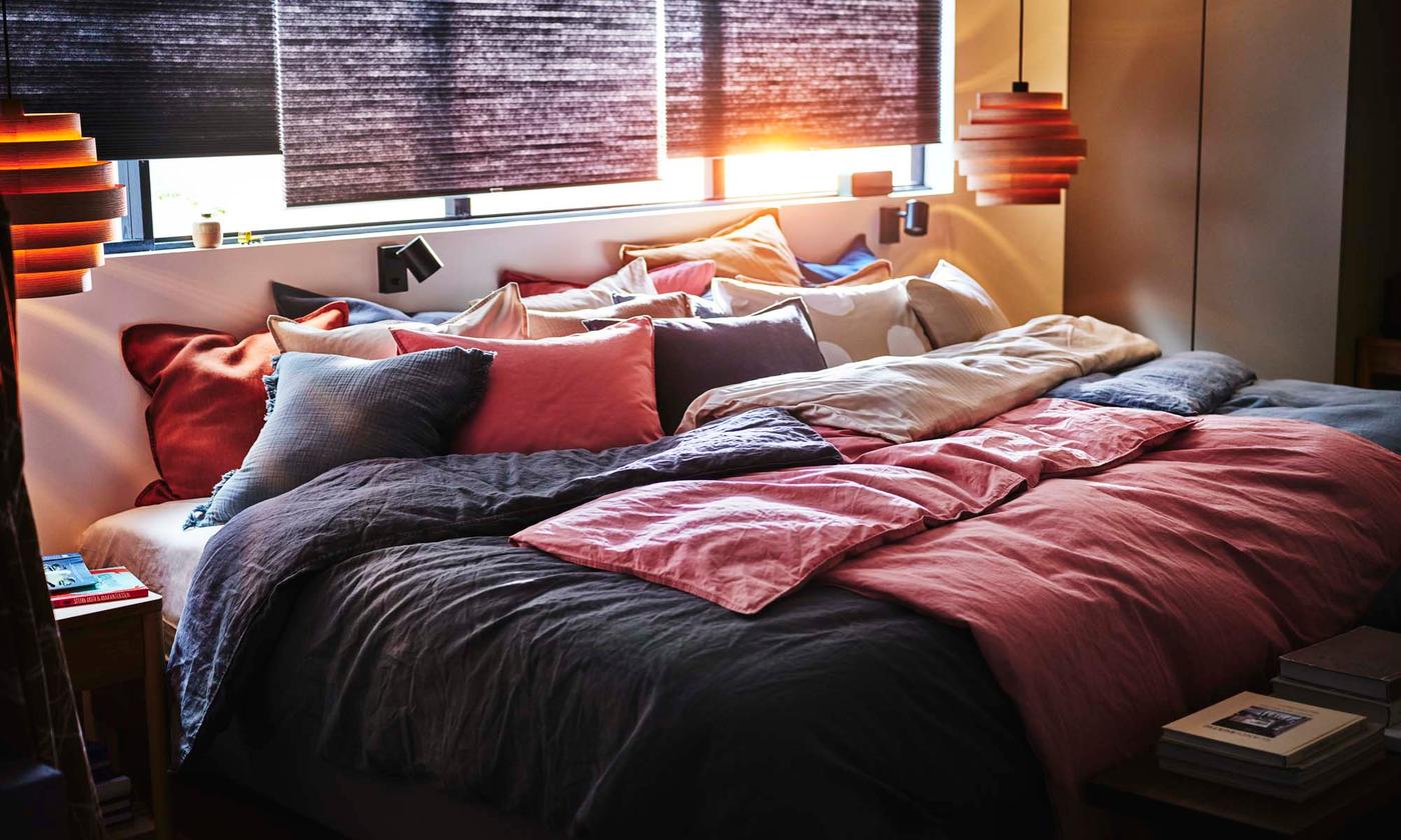 A bedroom with HOPPVALS room darkening cellular blinds behind a bed with dark pink ÄNGSLILJA and dark grey DYTÅG bedding.