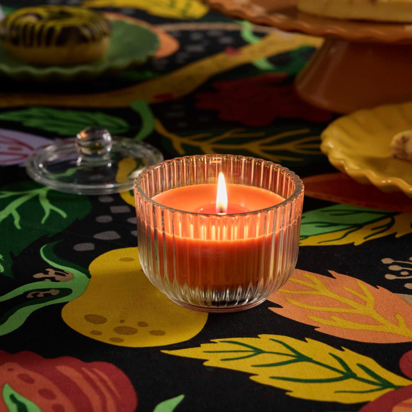 A sandalwood & patchouli orange HÖSTAGILLE scented candle in glass on a floral pattern multicolour HÖSTAGILLE tablecloth.