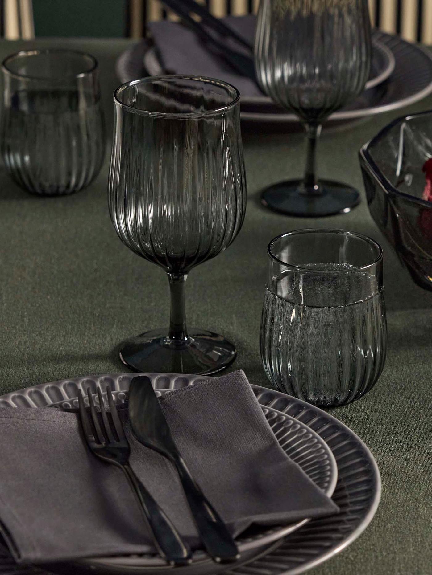 A table with grey stoneware STRIMMIG plates, HÖSTAGILLE glasses, wine glasses, and TILLAGD 24-piece cutlery.