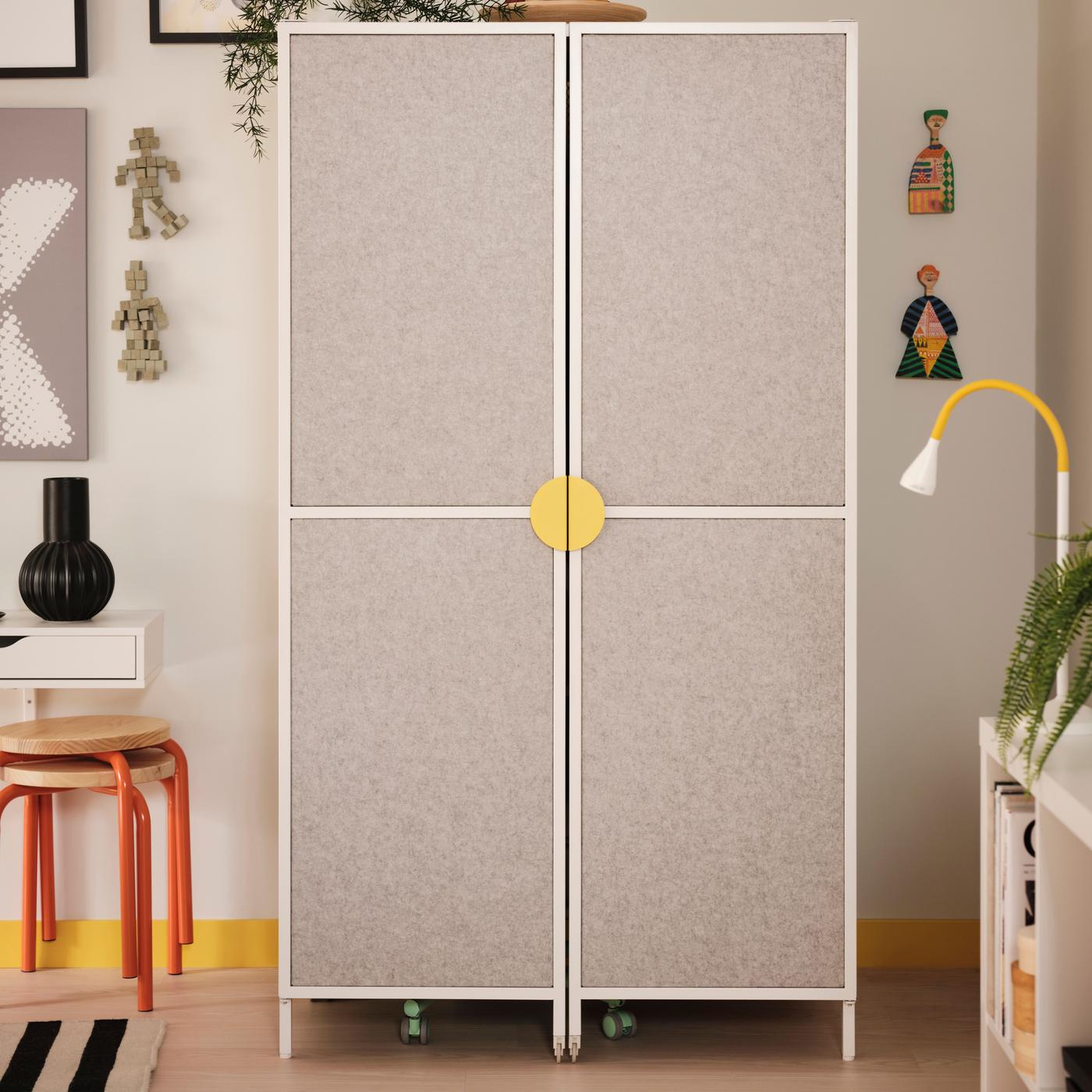 A white cabinet with a yellow knob is standing in a bright white room next to the wall. Doors are closed.