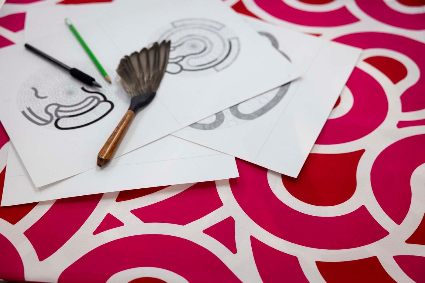 A pile of drawings and brushes on a patterned tablecloth.