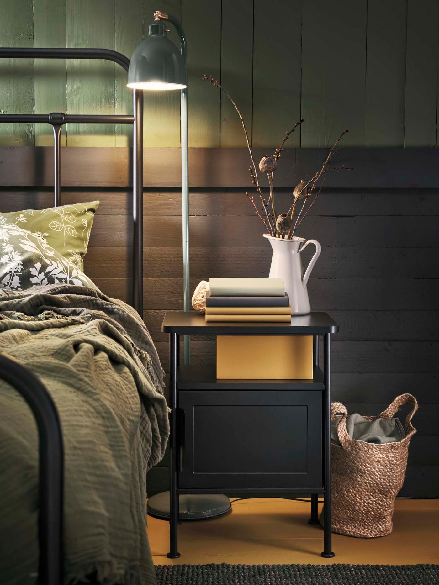 A green industrial-style floor lamp beside the bed in a dark green bedroom.