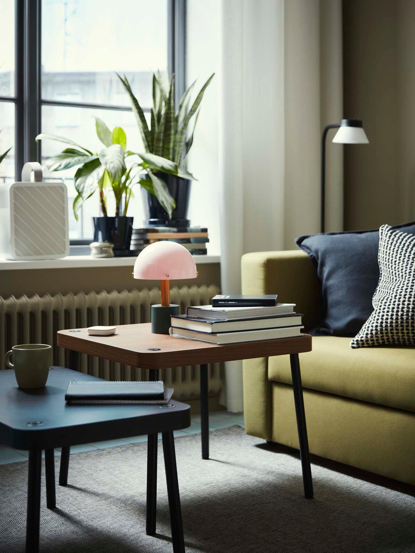 A pink and green portable table lamp rests on a wooden coffee table in a green and white living room.