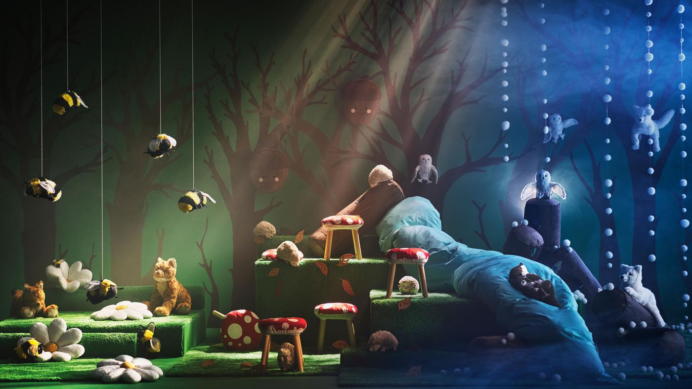 A scene where the SKOGSDUVA collection is displayed on a Swedish forest backdrop. Different soft toys like the bees, owls, arctic fox, lynx, otters and hedge hocks are shown, as well the toad stools, duvet covers, flower and acorn cushions.