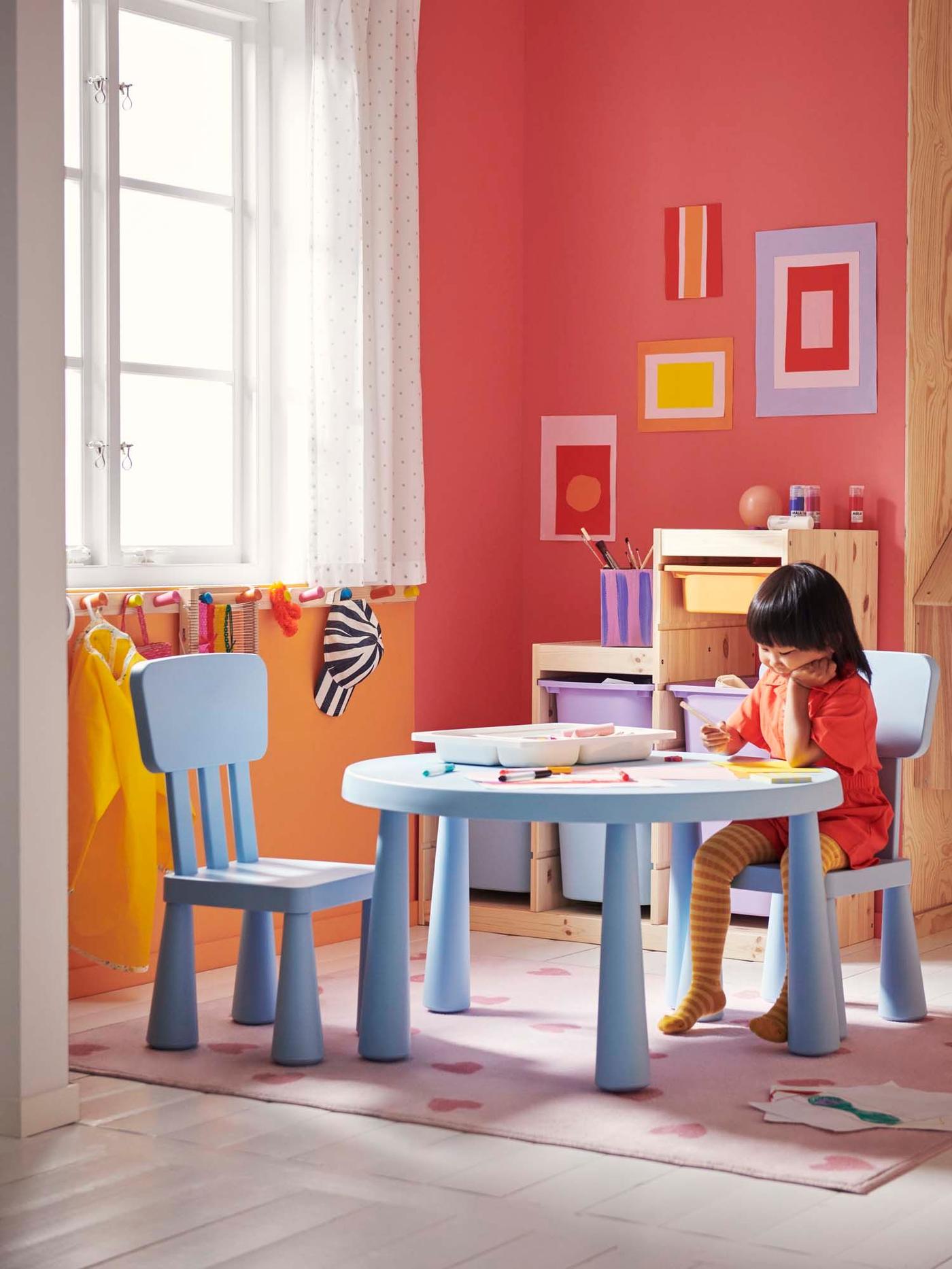 A child sits at a light blue MAMMUT table and draws, in a pink children's room.