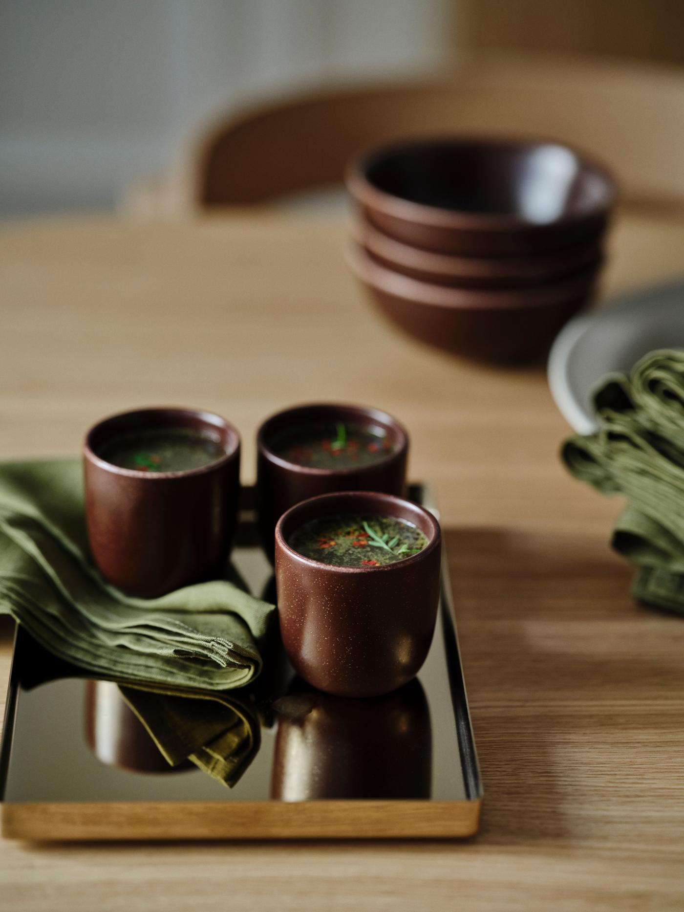 Glazed stoneware mugs with tea and plates on a wooden tray, placed on a wooden table with green linen napkins.
