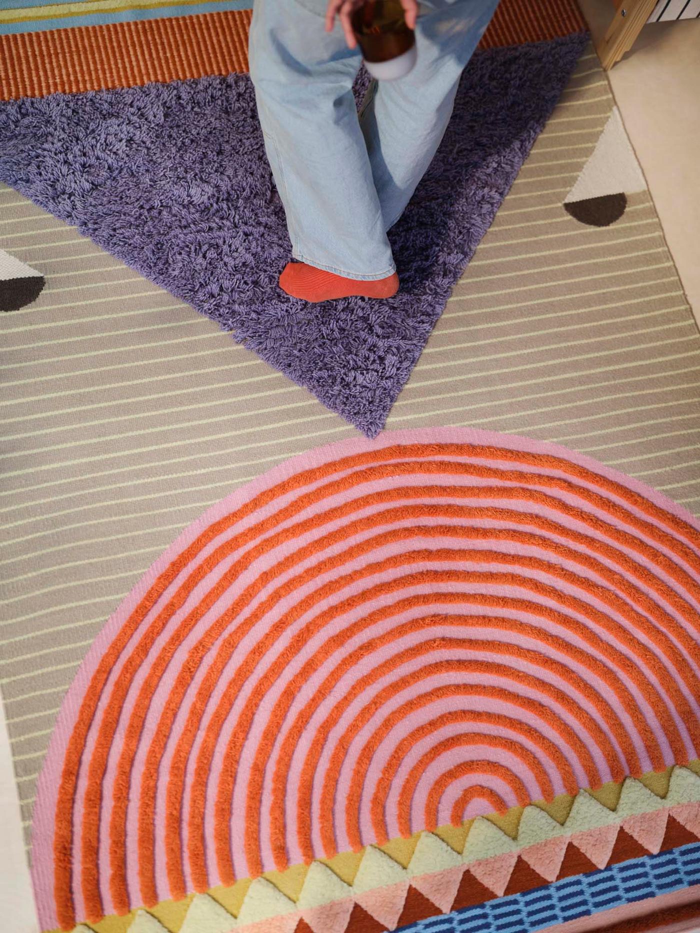 An aerial view of an OMMJÄNGE rug, with a pair of legs standing on the rug.