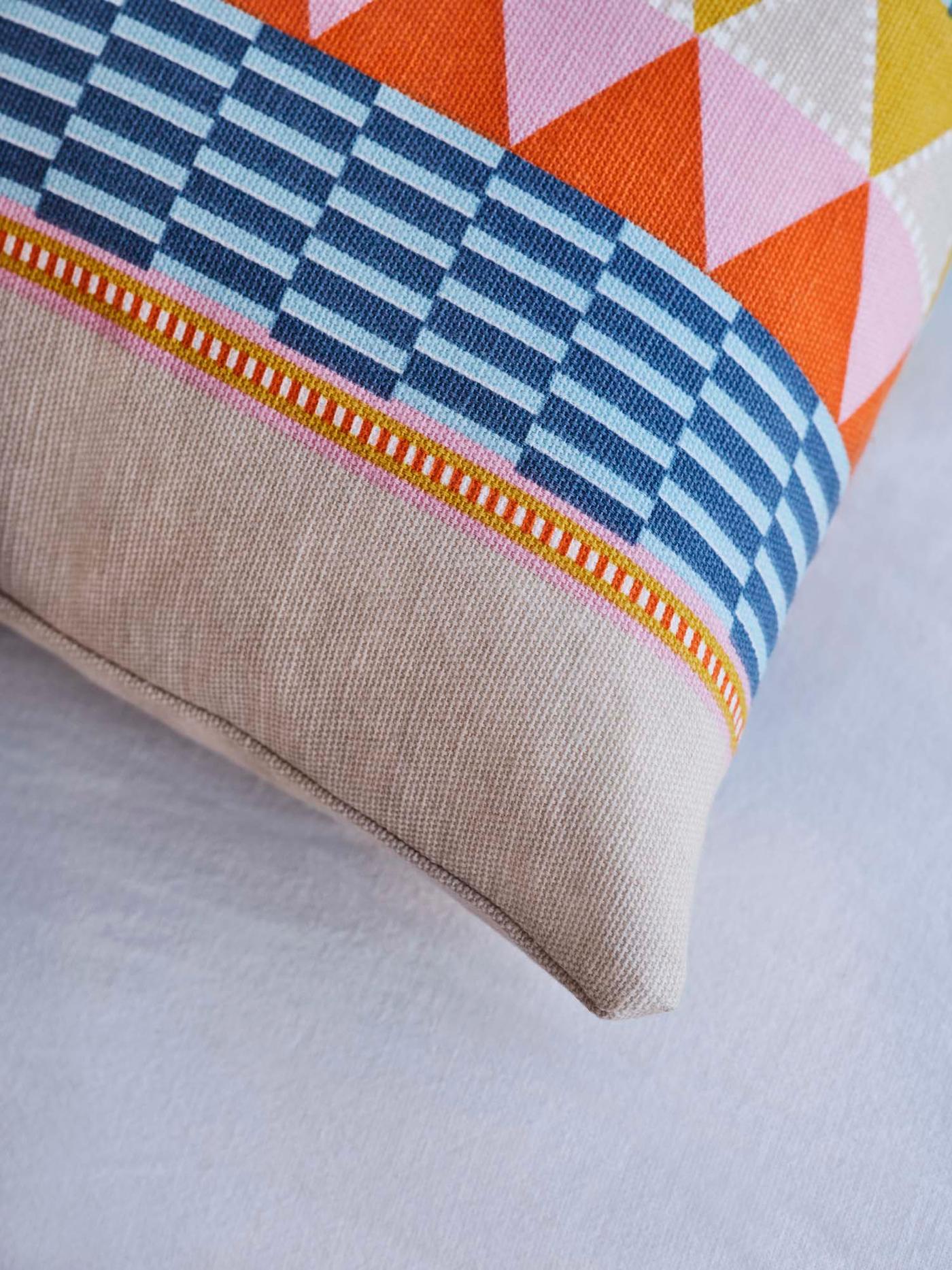 The corner of a colourful, patterned OMMJÄNGE cushion on a white bed.