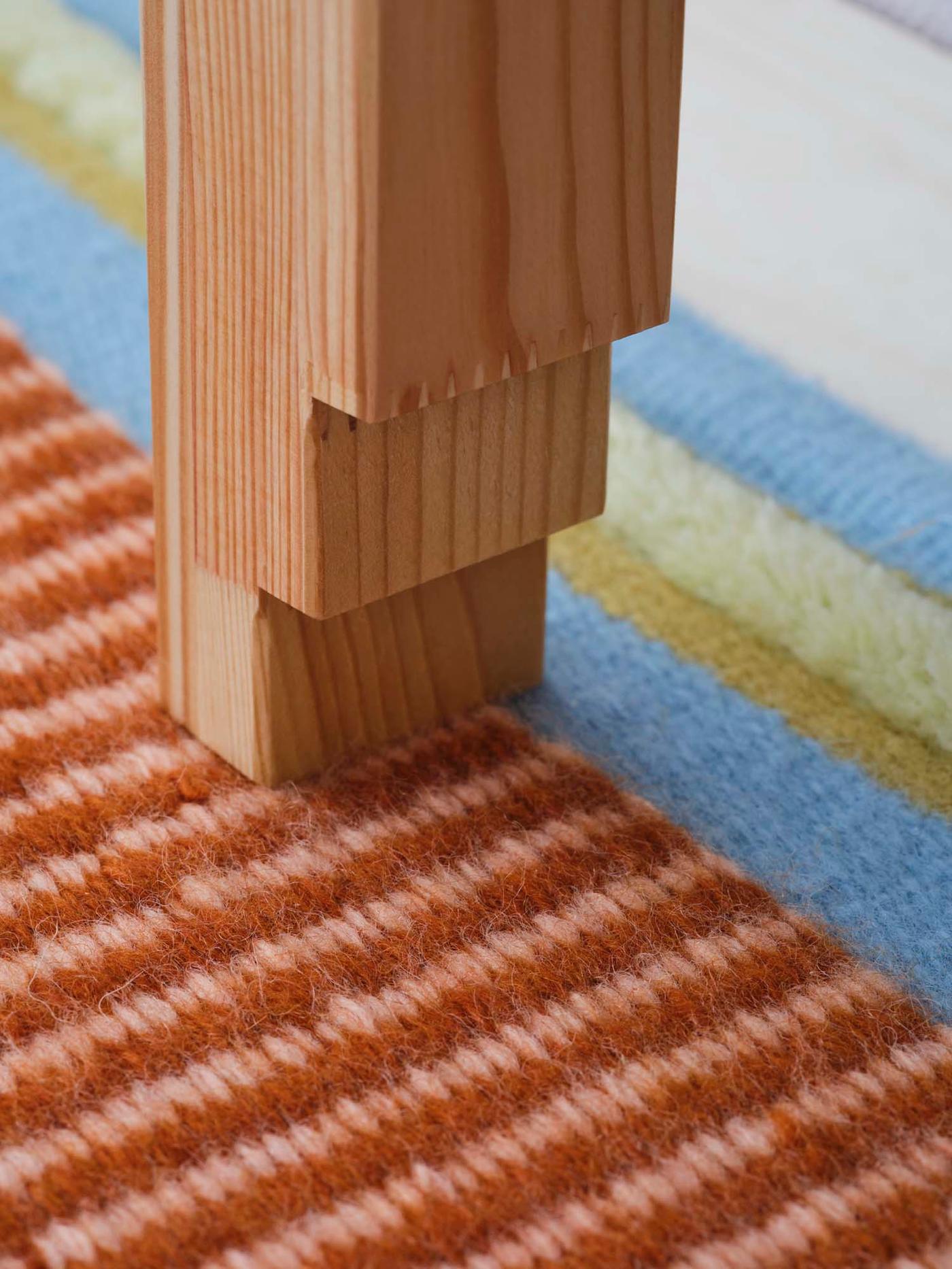 A close-up of a wooden OMMJÄNGE bench leg on a colourful rug.