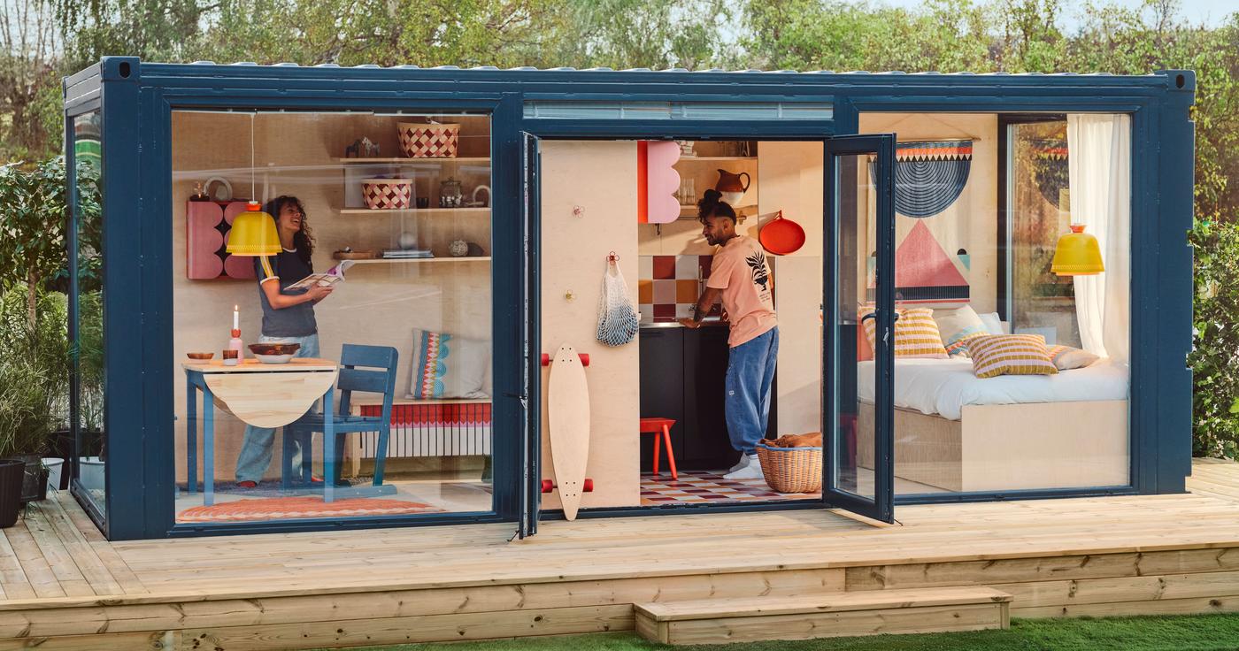 Two people in a cabin-like container house, surrounded by modern, bright, Scandinavian style furniture.
