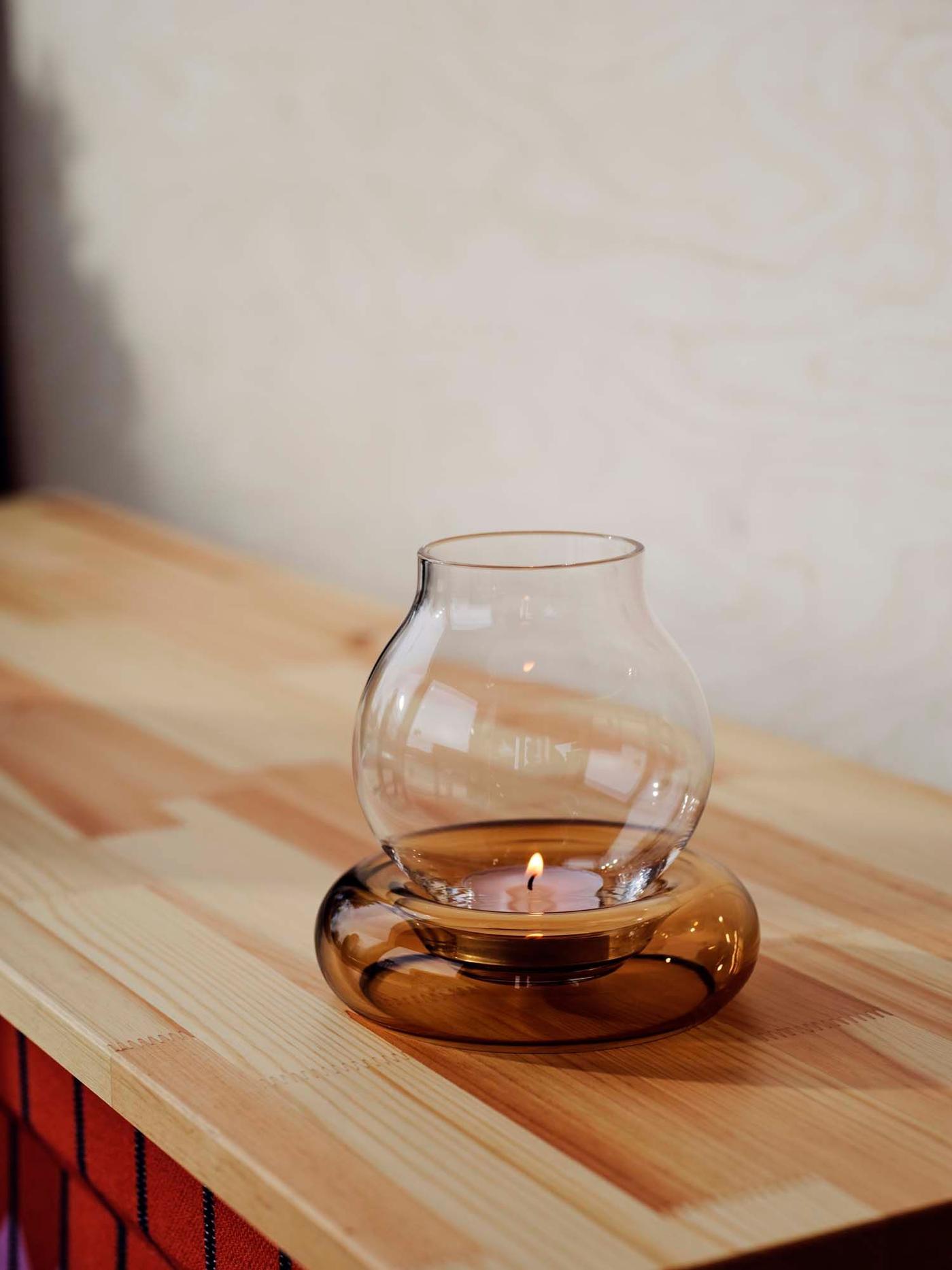 A glass OMMJÄNGE tealight holder on a wooden shelf.