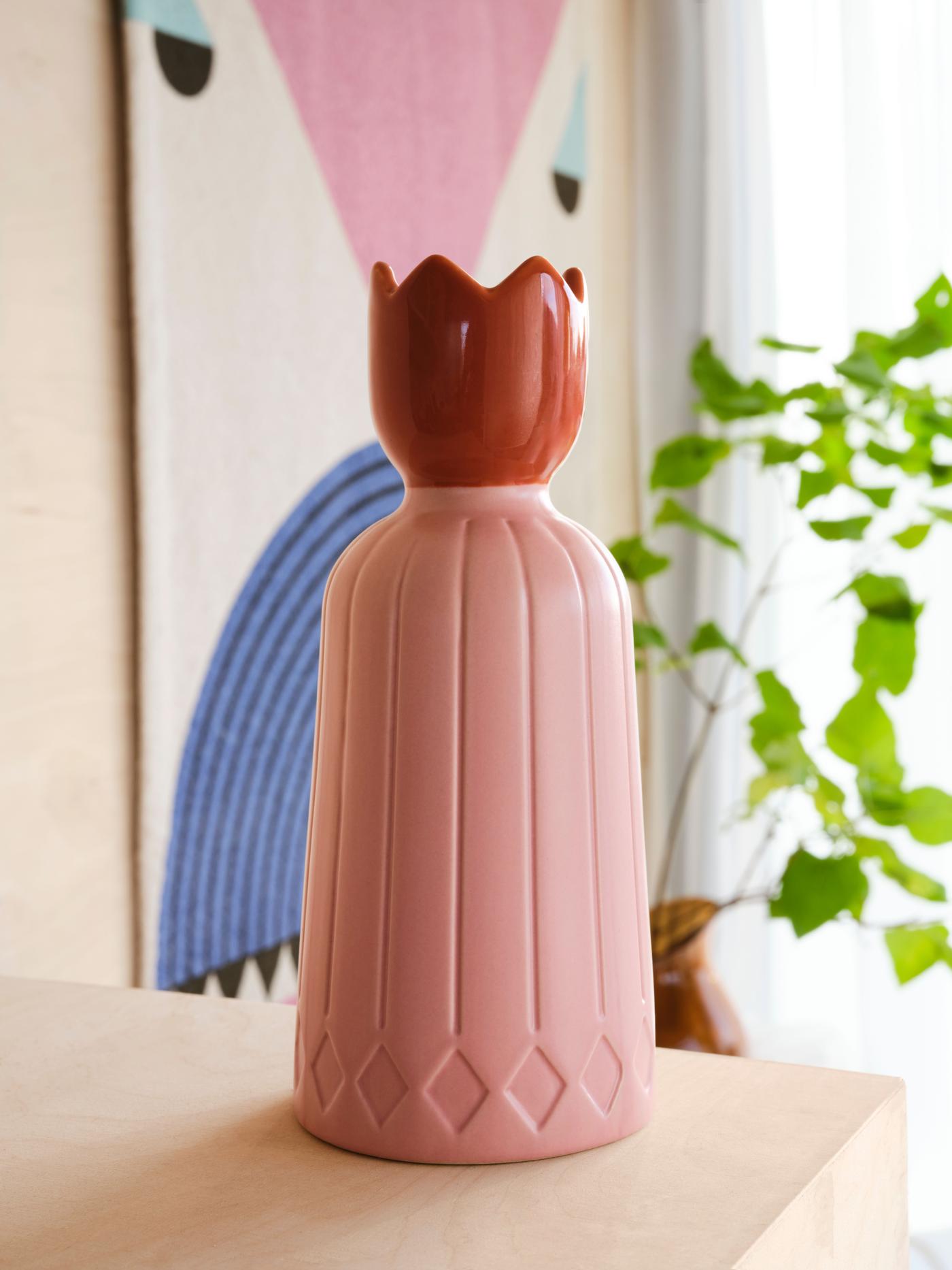 A pink and red candle holder sits on a wood shelf with a plant and picture behind.