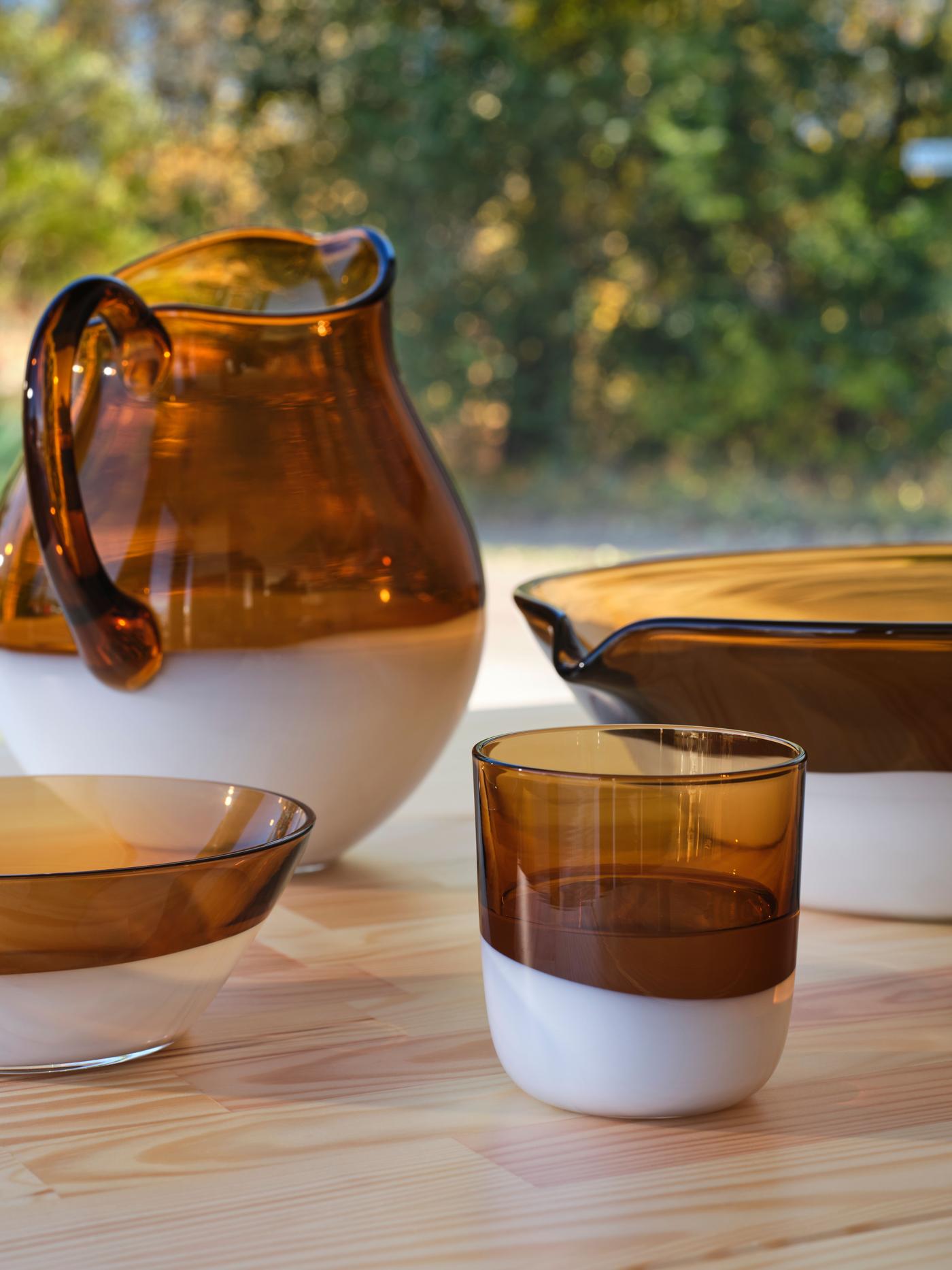 A jug, tumbler and bowls in half brown glass and half white glass.