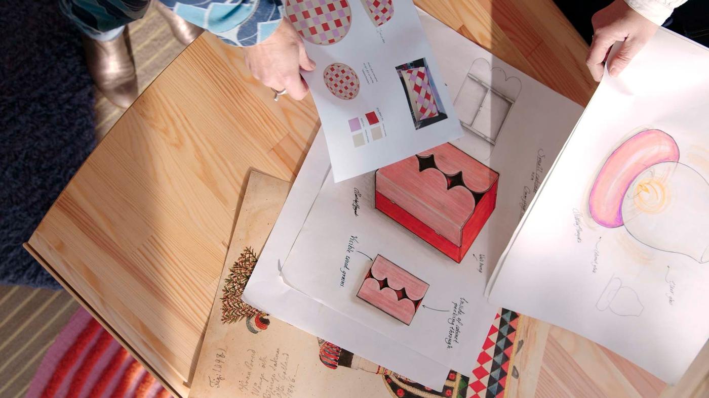 An aerial view of hands holding sketches of products from the OMMJÄNGE collection, over a wood table.
