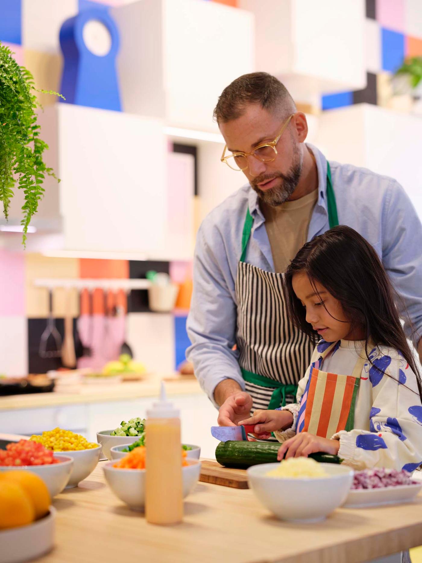 A parent and child chopping vegetables together in a bright coloured kitchen.