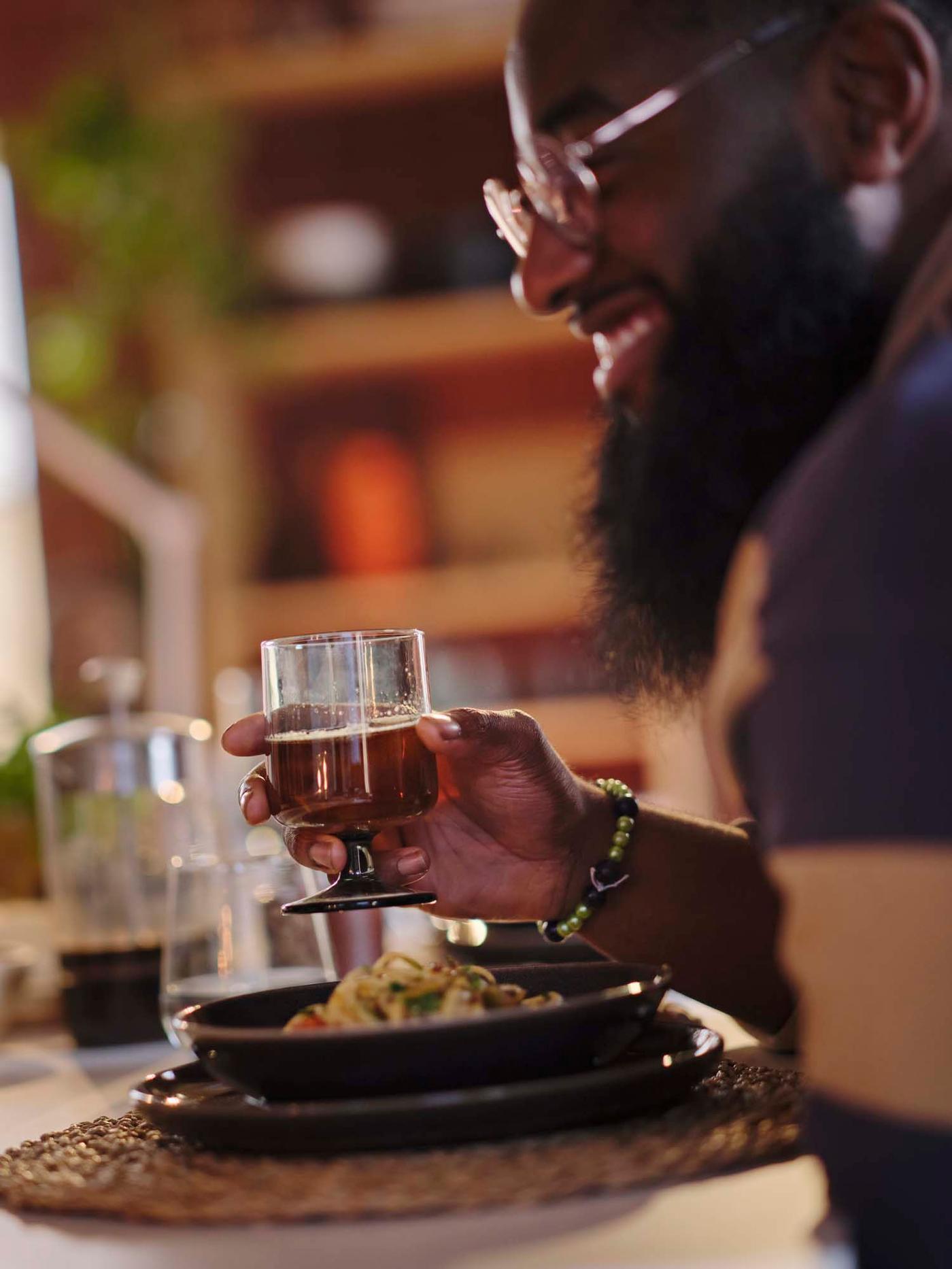 A person smiles as they enjoy a bowl of pasta served in rustic brown STOCKHOLM 2025 stoneware.