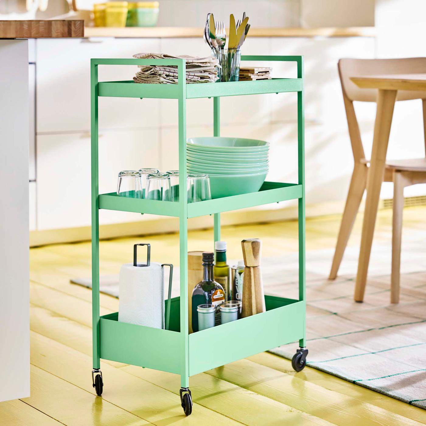 A green trolley loaded with dinnerware in a yellow and white kitchen.