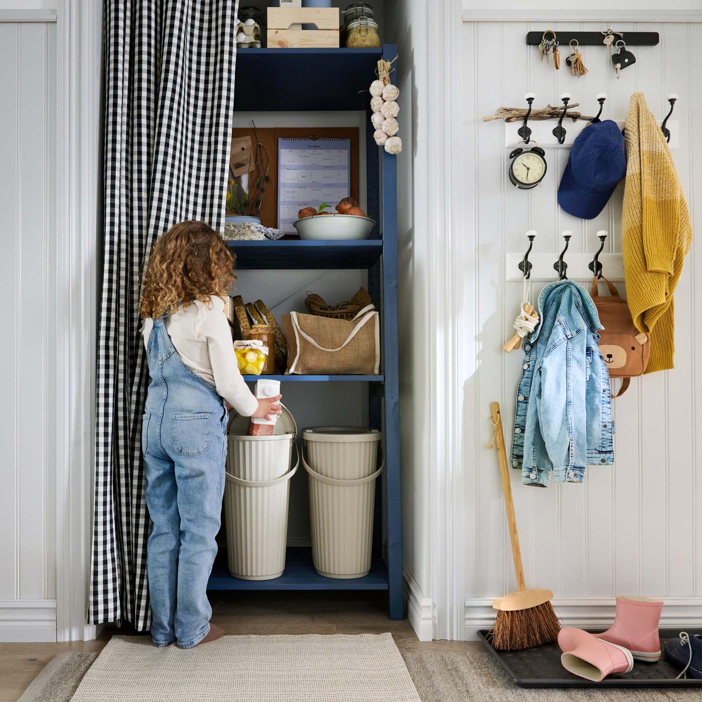 A child puts recycling objects into DAMMÄNG recycling bins behind a curtain in the hallway.
