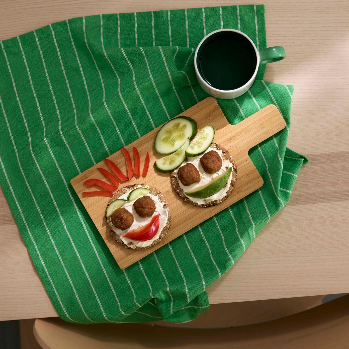 Round open sandwiches designed to look like faces on a wood chopping board with a green tea towel under.
