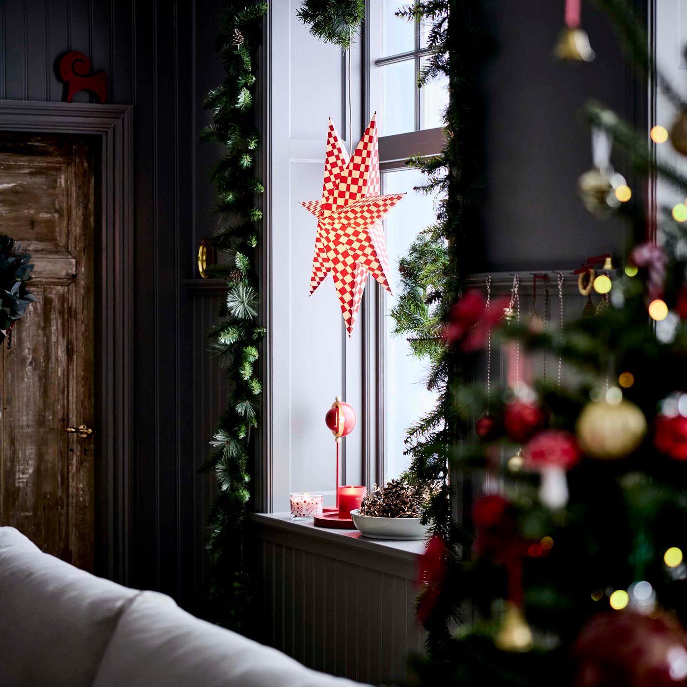 A red and white star lamp in the window of a dark coloured living room at Christmas time.