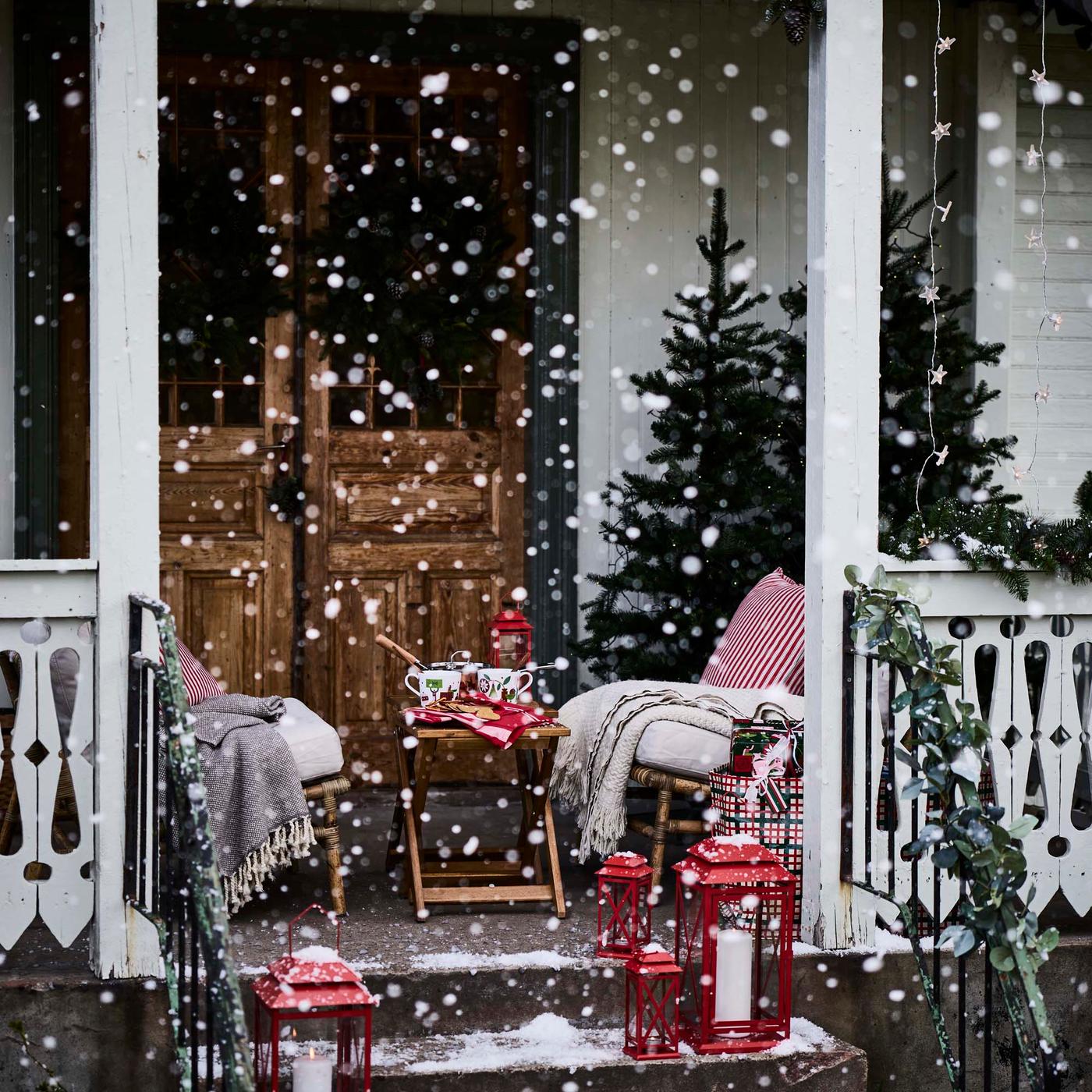 A front porch in the snow at Christmas time with red lanterns and seating draped in blankets.