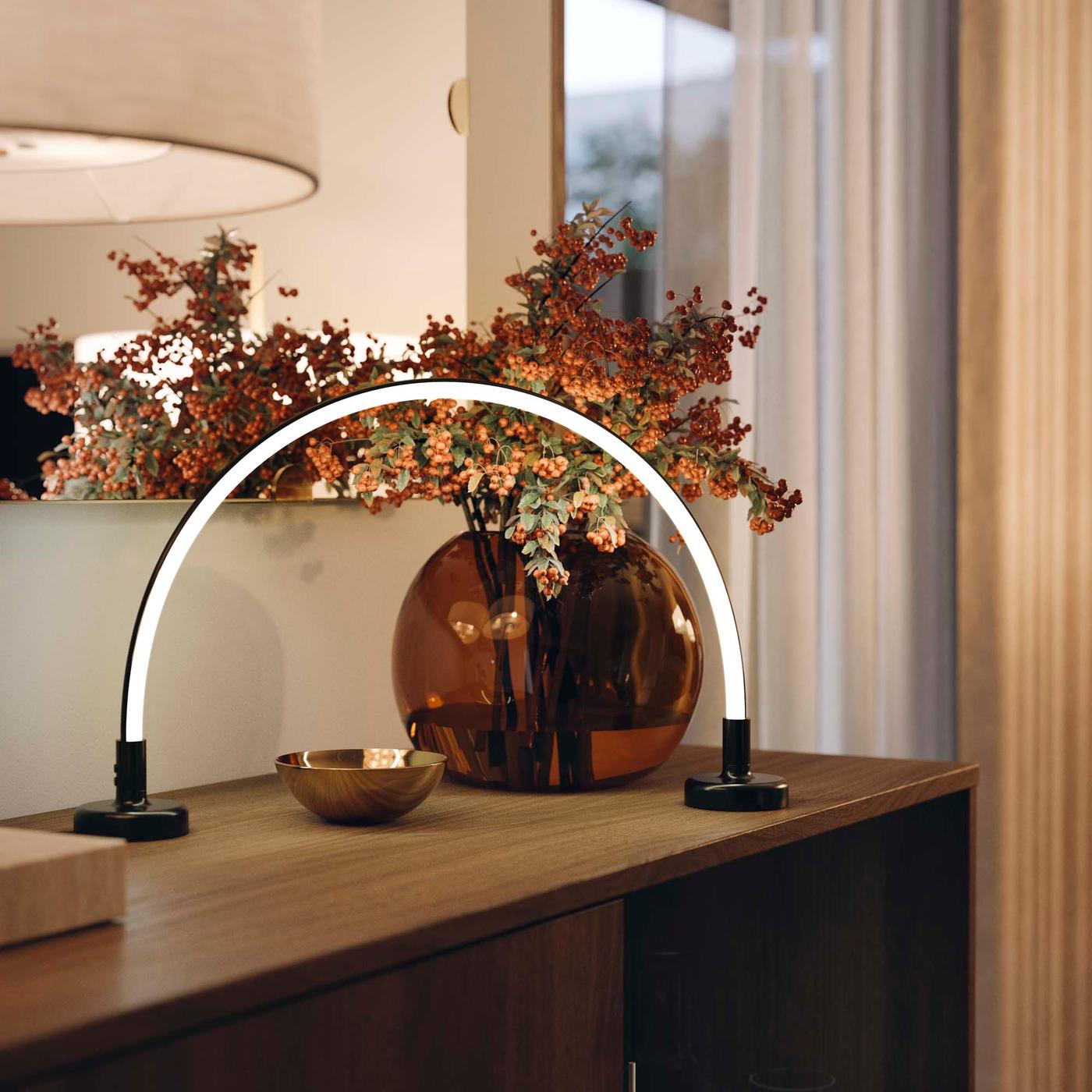 An arc-shaped shaped black lamp with a white light rests on a wooden side table.