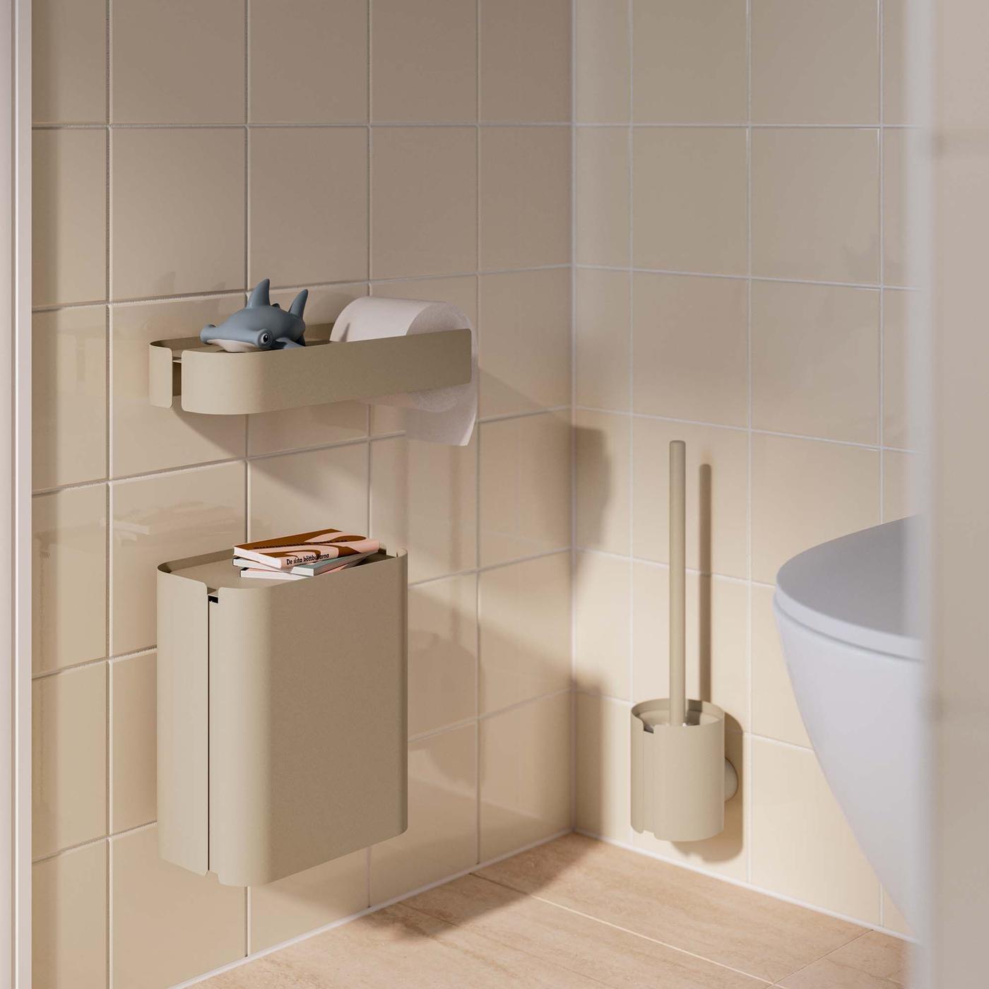 A beige WC with a wall-hung bin, shelf and toilet brush next to a toilet.