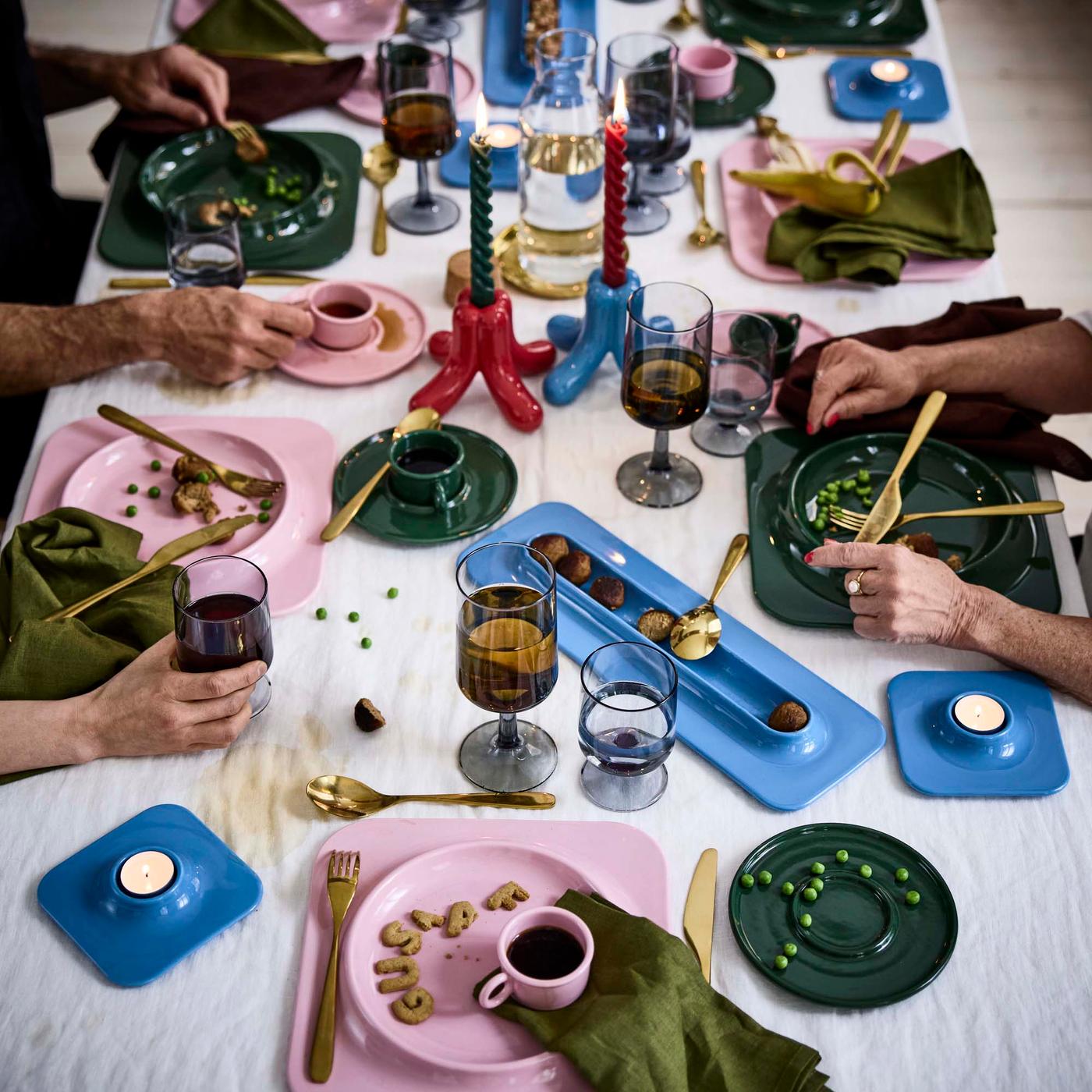 A closeup on a festive table setting which includes colourful ceramic pieces in red, pink, green and blue and gold-tone flatware.