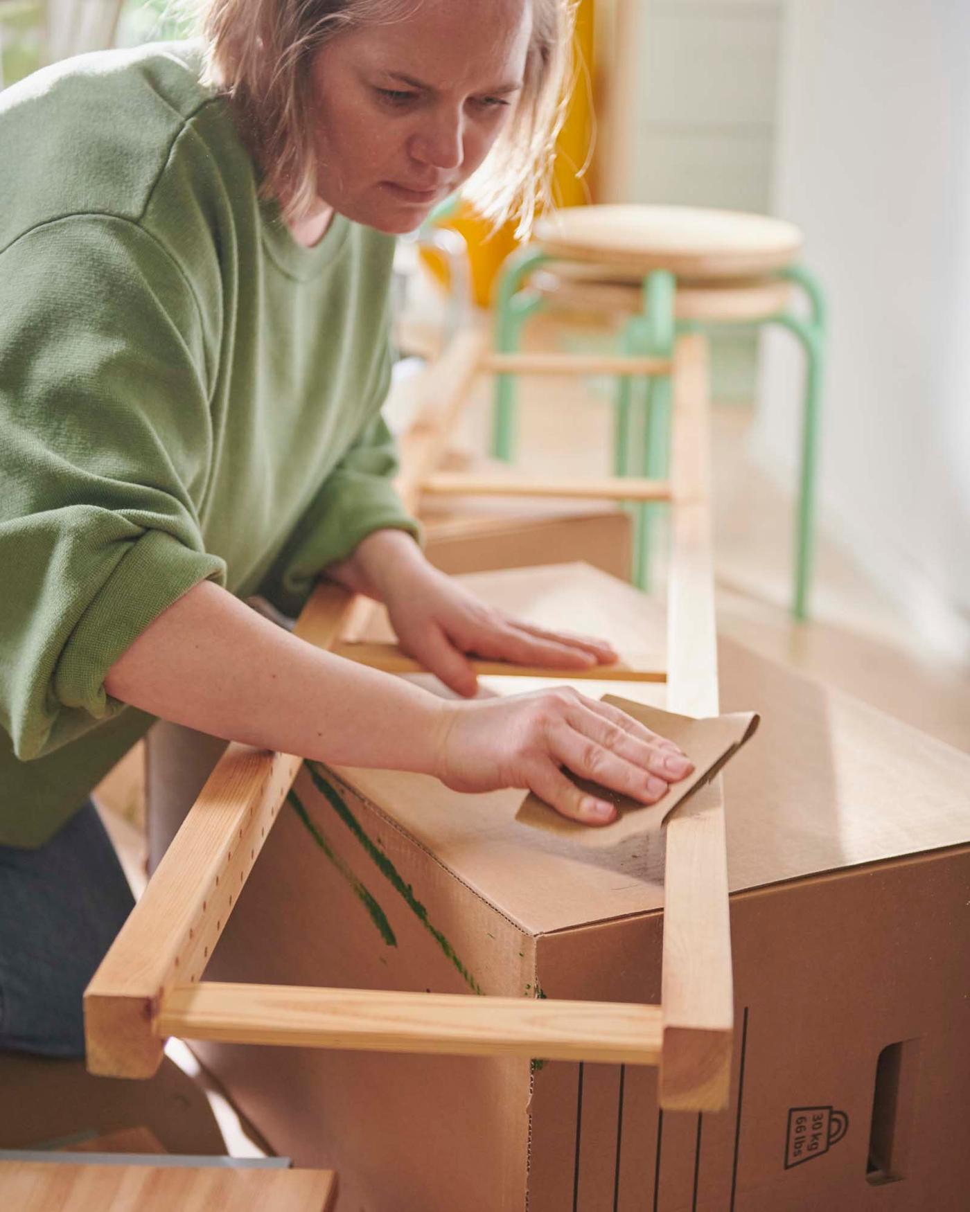 A person lightly sanding an IVAR cabinet side unit.