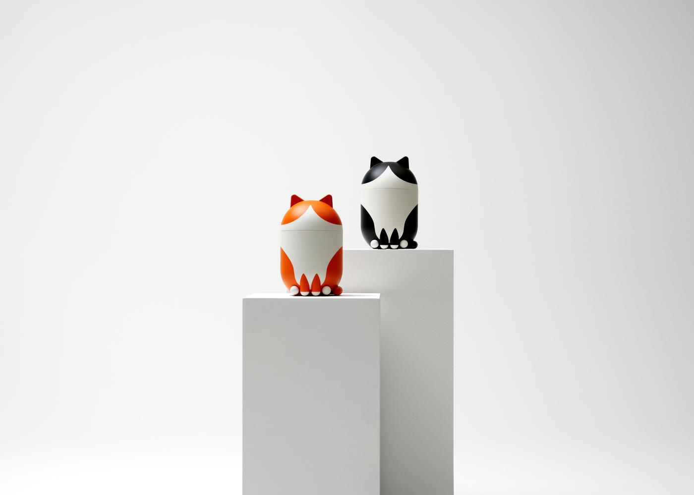 Two cat-shaped decorative storage jars standing on a white pedestal against a white background.
