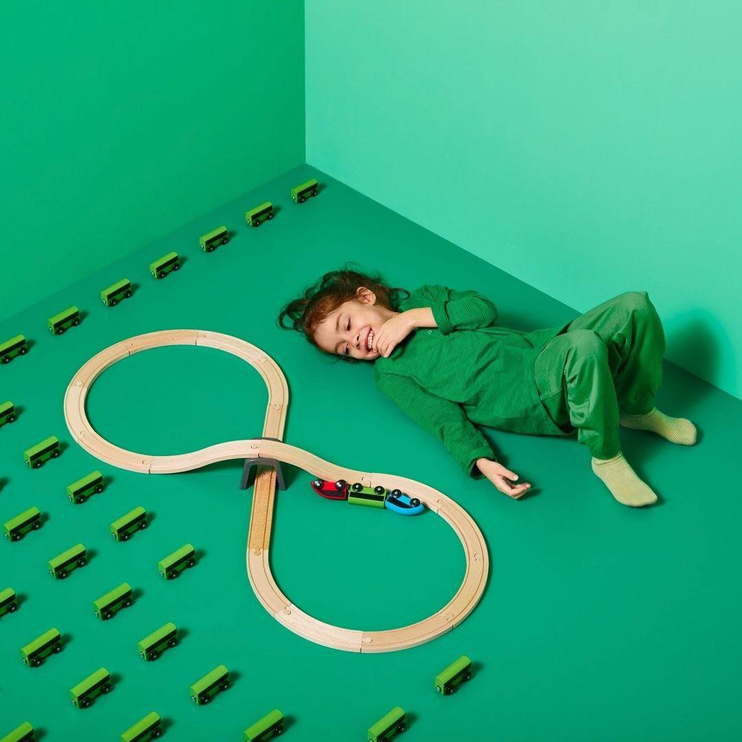 A child lying on a green floor next to toy train track.