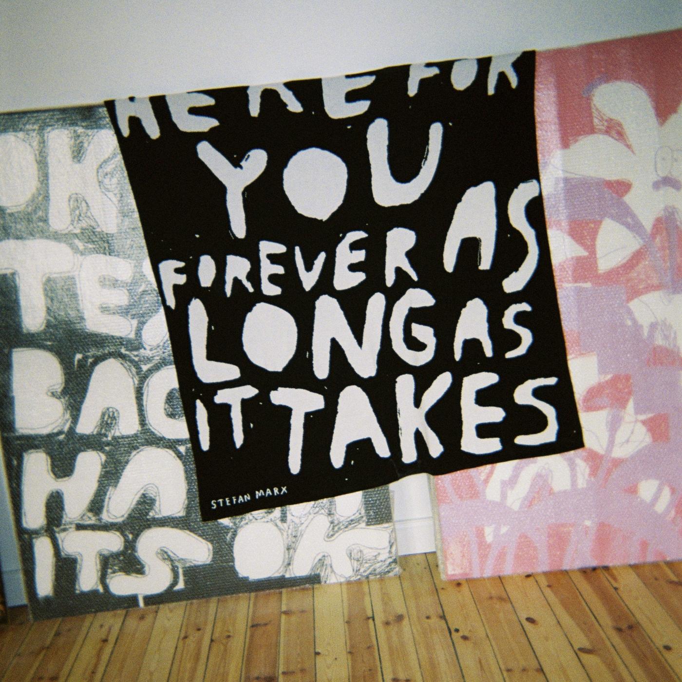 A green and a black piece of fabric with large white lettering, beside a pink/violet piece of fabric with a floral pattern.