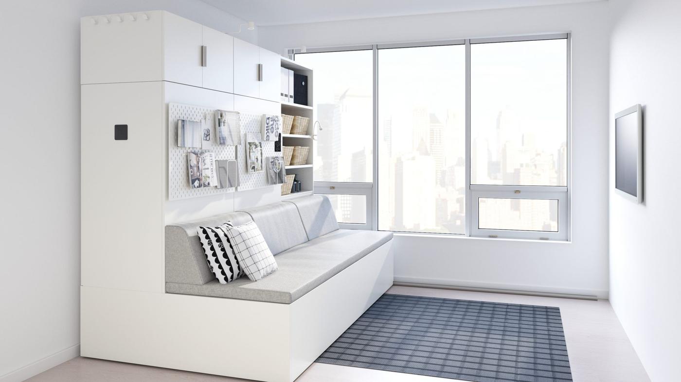 A large white piece of furniture on one side of a white room, with a grey sofa and white storage built in.