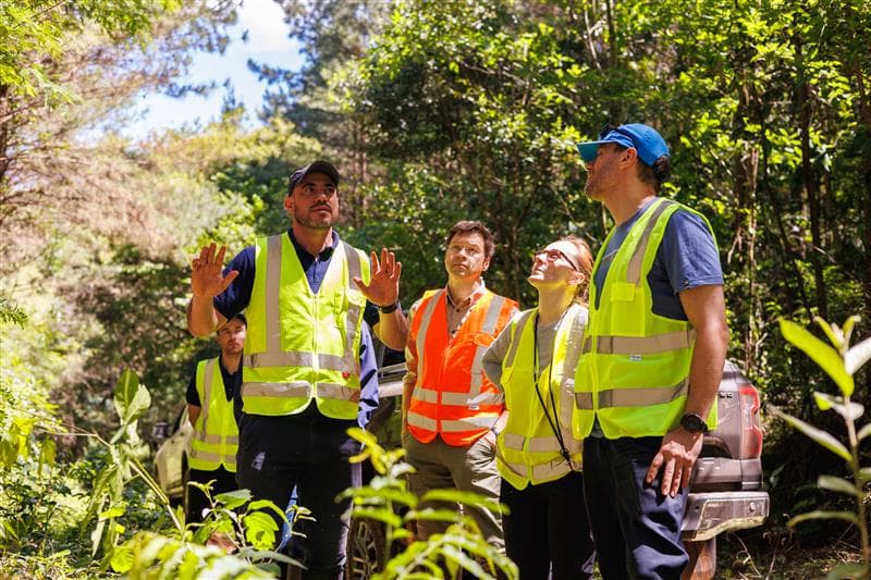 A group of people in reflective vests stand and talk in a lush, green area in Brazil.