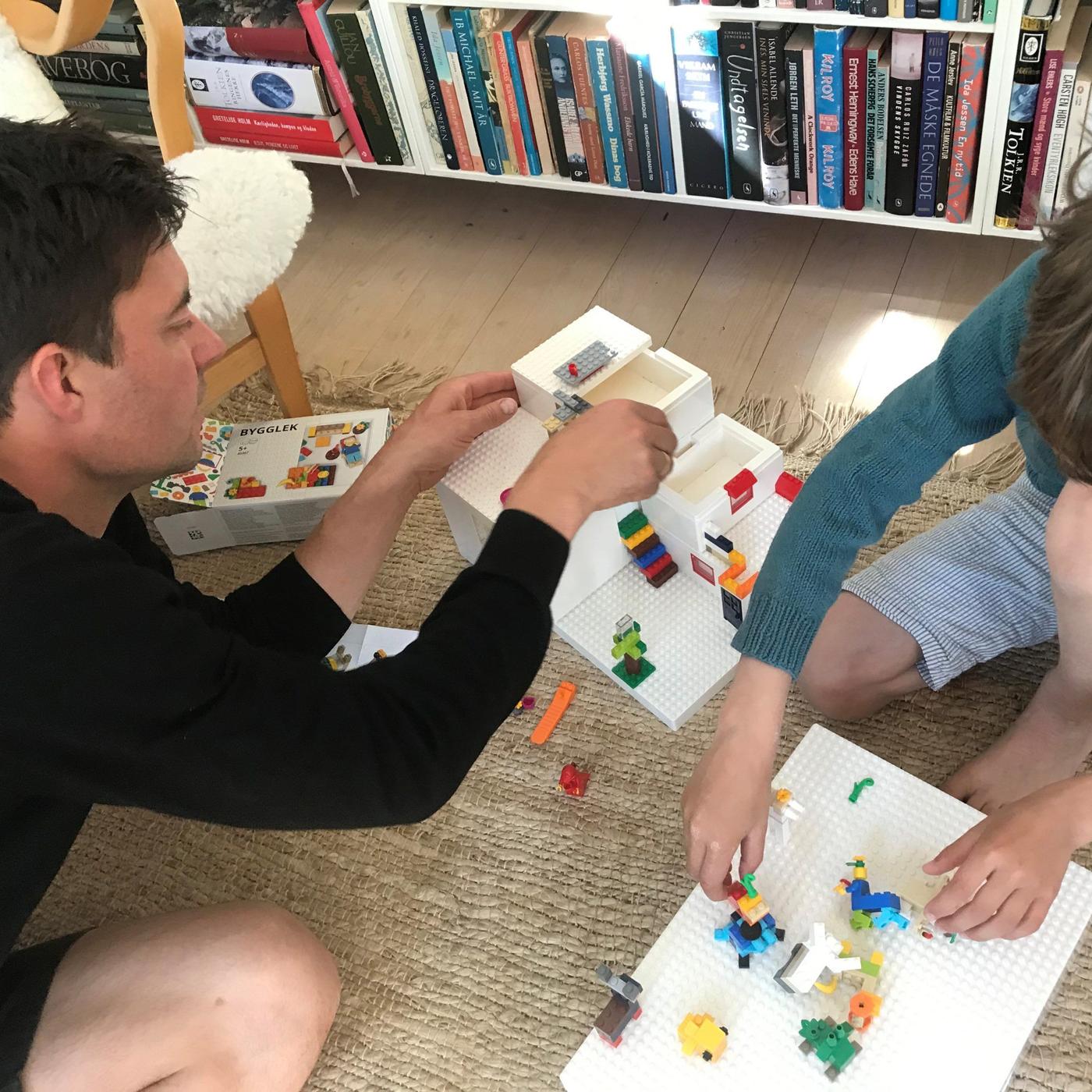 Two men playing with BYGGLEK LEGO boxes on the floor.