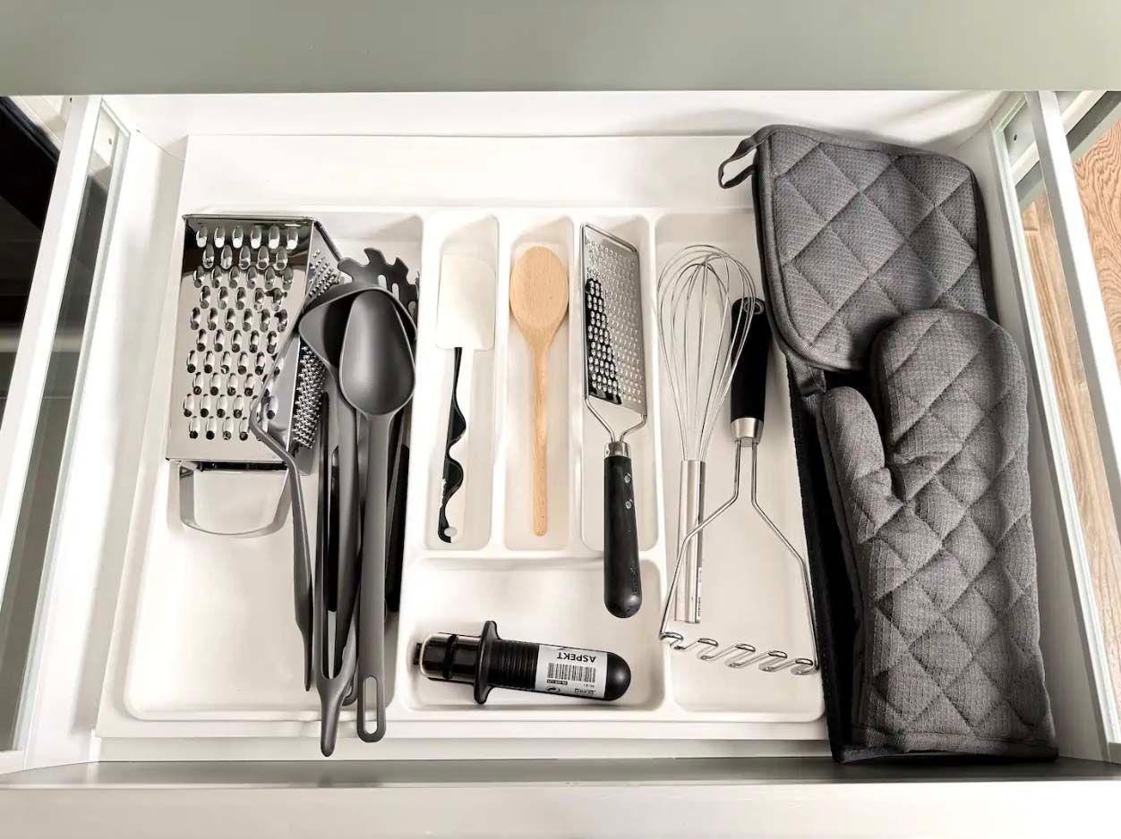 An open kitchen drawer revealing cutlery, kitchen utensils and oven gloves.