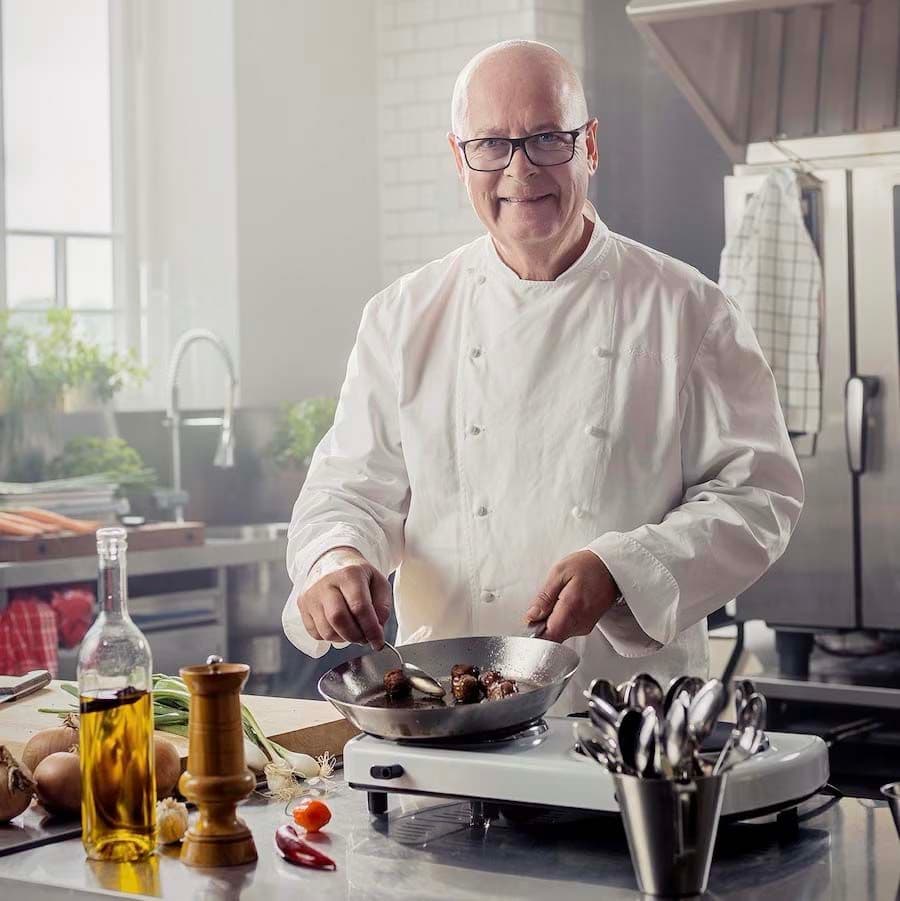 Chef Severin Sjöstedt stands in a kitchen. He smiles at the camera as he cooks meatballs.