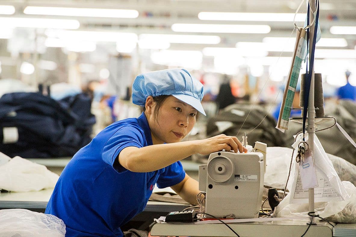 A person in a factory setting works at a sewing machine.