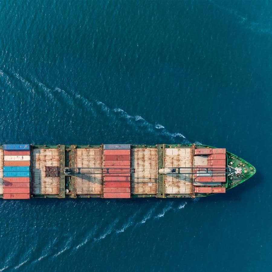 A cargo ship shot from above makes its way across a still, blue ocean.