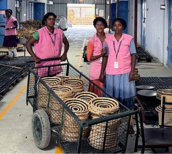 Three people stand in the workplace, in front of a trolley with rattan baskets.