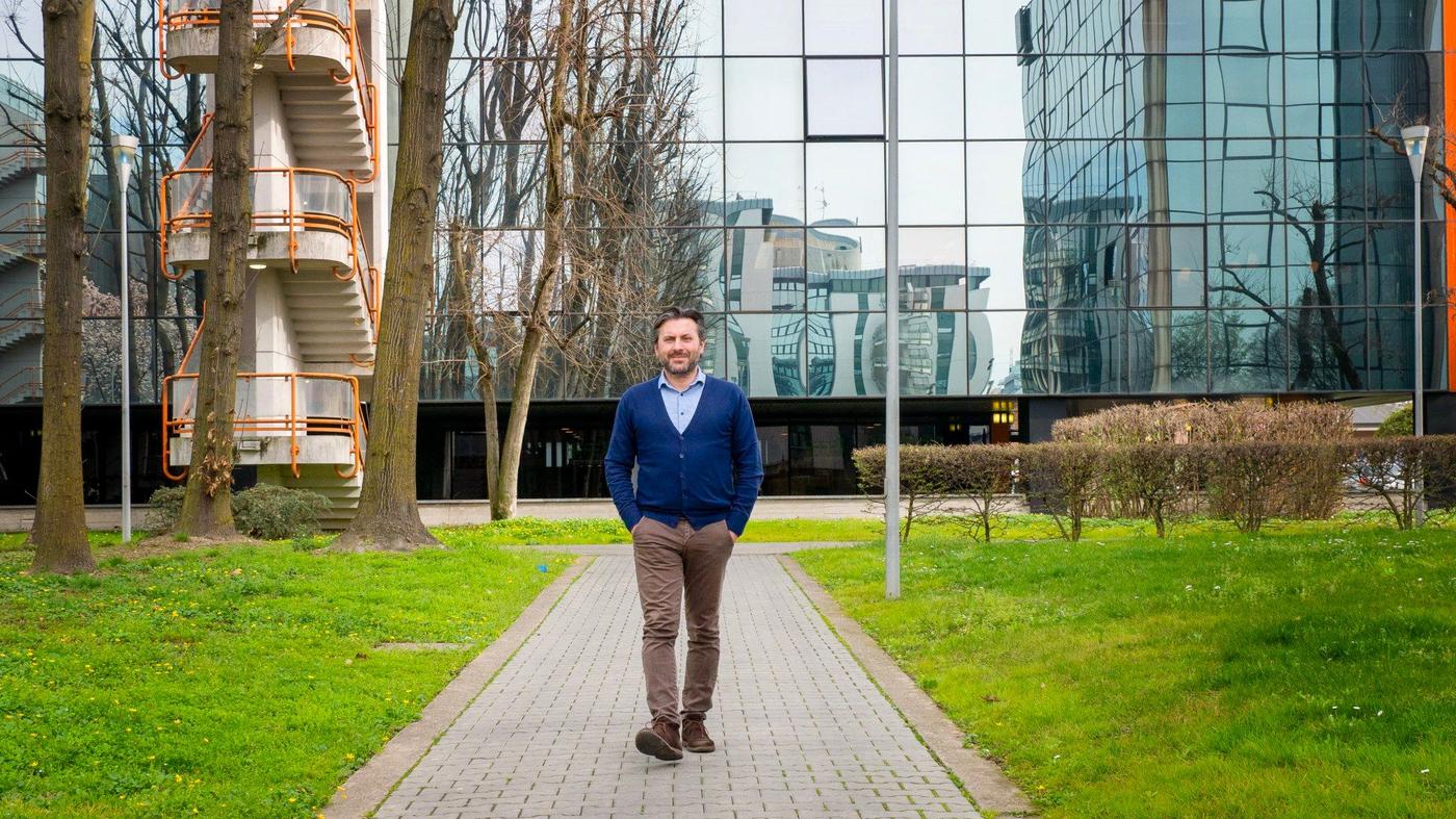 A man with his hands in his pockets walking in front of an office building.